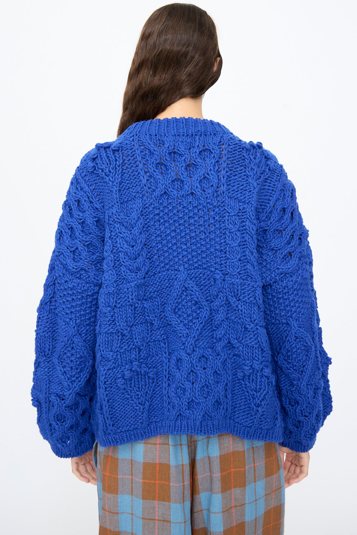 Back view of a person wearing an oversized, bright blue Wool Hand Knit Pullover in Blue paired with plaid trousers.