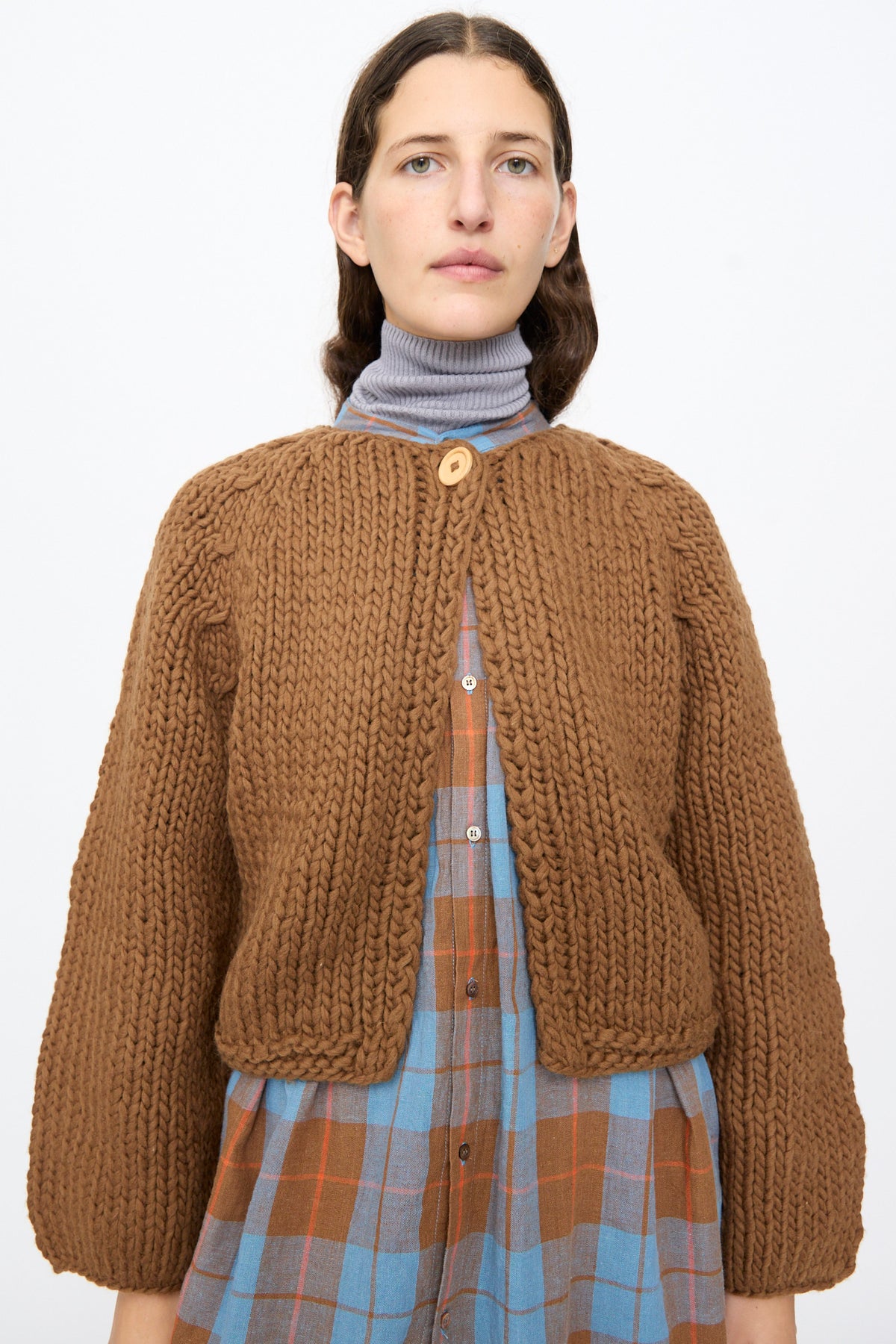 Ichi Antiquités Wool Hand Knit Pullover in brown, cropped with a single wooden button closure, worn over a blue plaid shirt and grey turtleneck.
