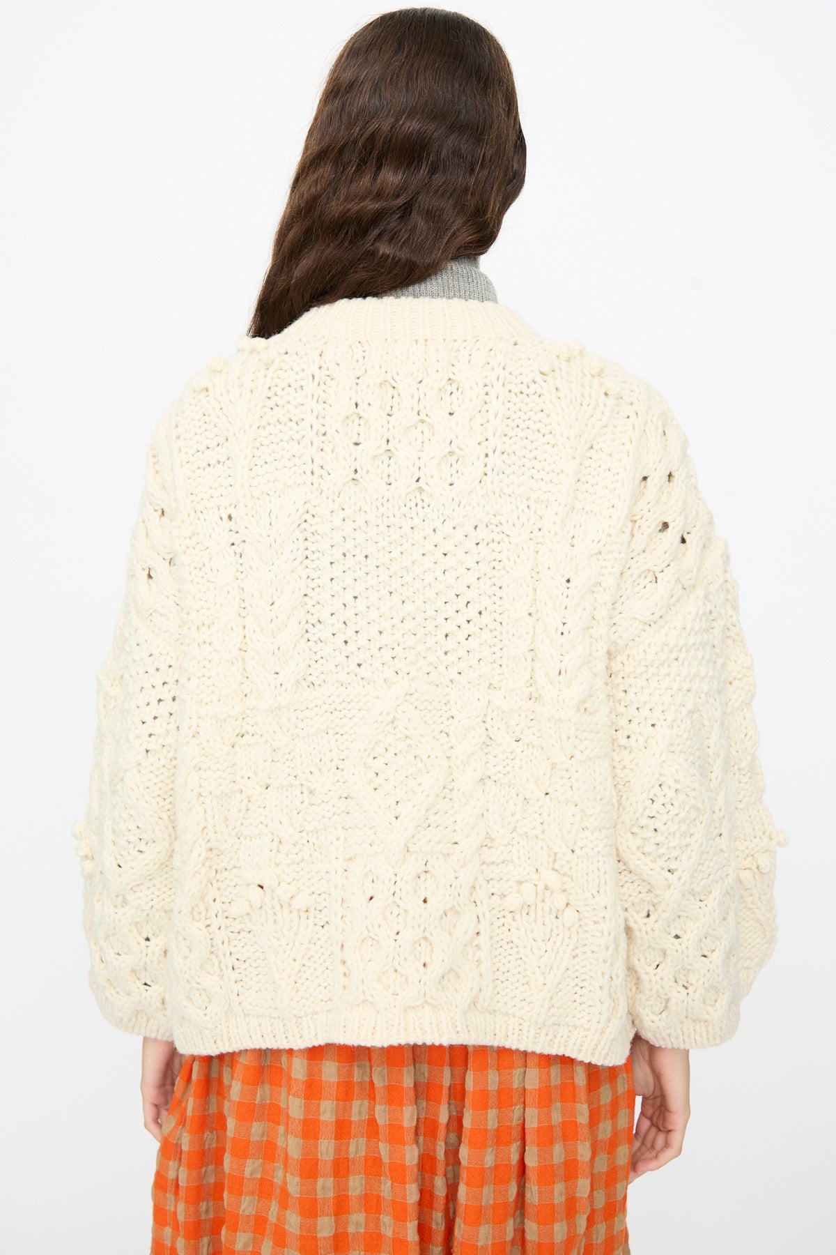 Back view of an oversized, cream-colored Wool Hand Knit Pullover in White by Ichi Antiquités worn over an orange and beige checkered dress.