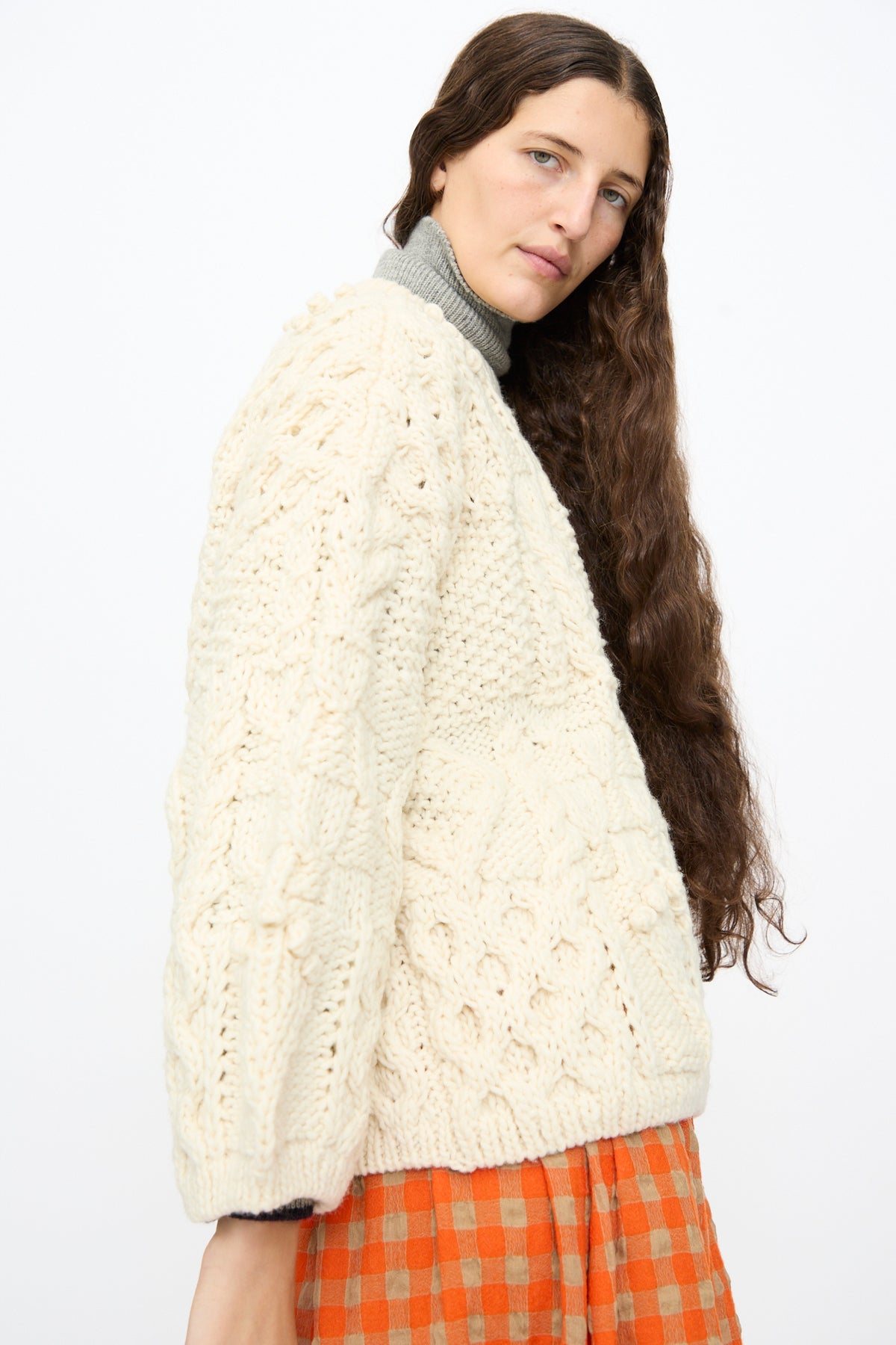 A person wearing an Ichi Antiquités Wool Hand Knit Pullover in White over a gray turtleneck and a red and tan checkered skirt.