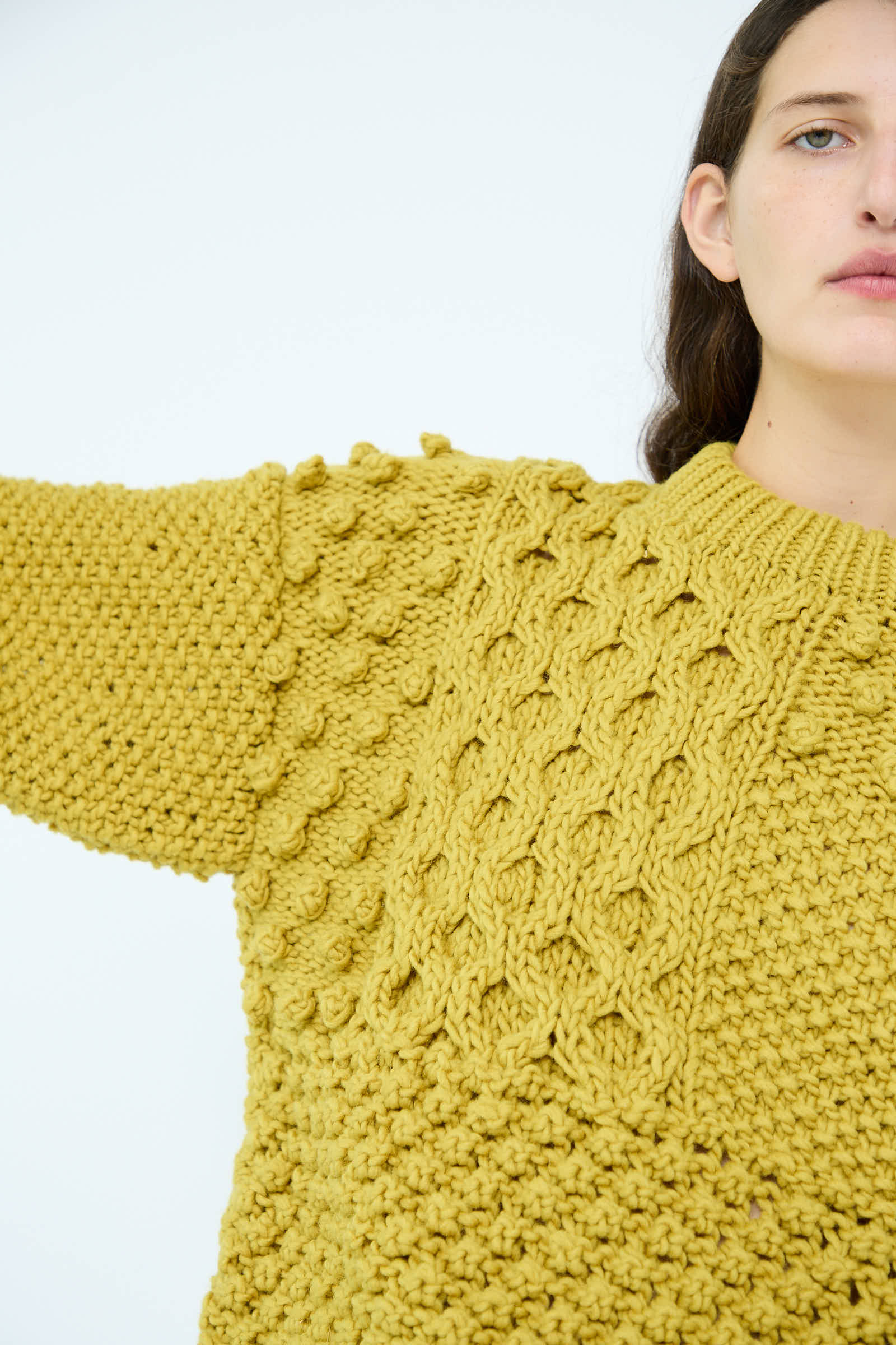 A person wearing the Wool Hand Knit Pullover in Yellow by Ichi Antiquités, partially raising their arm against a white background.