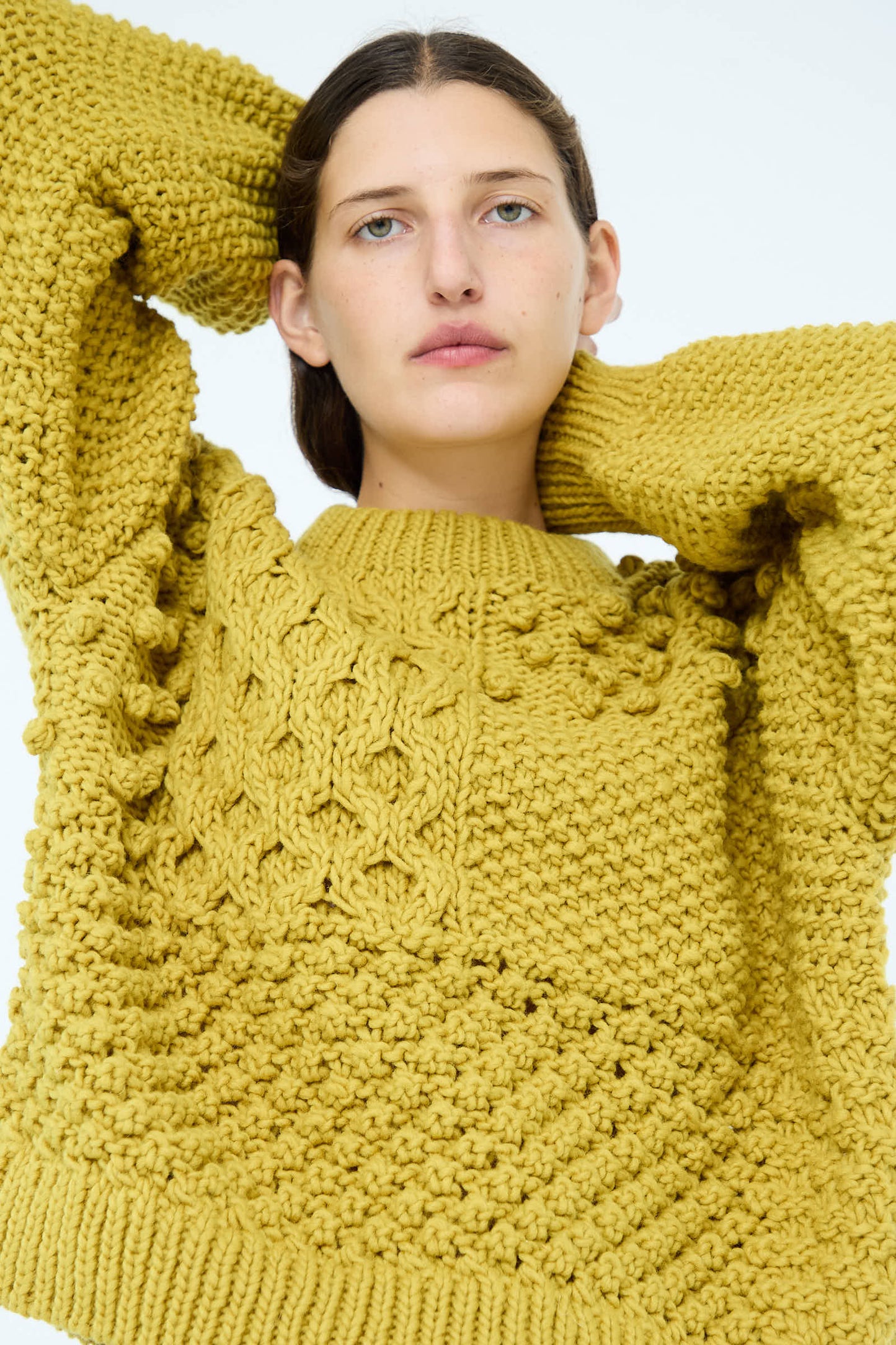 A person is wearing the Wool Hand Knit Pullover in Yellow by Ichi Antiquités, with a textured design made from 100% wool, their arms raised above their head.