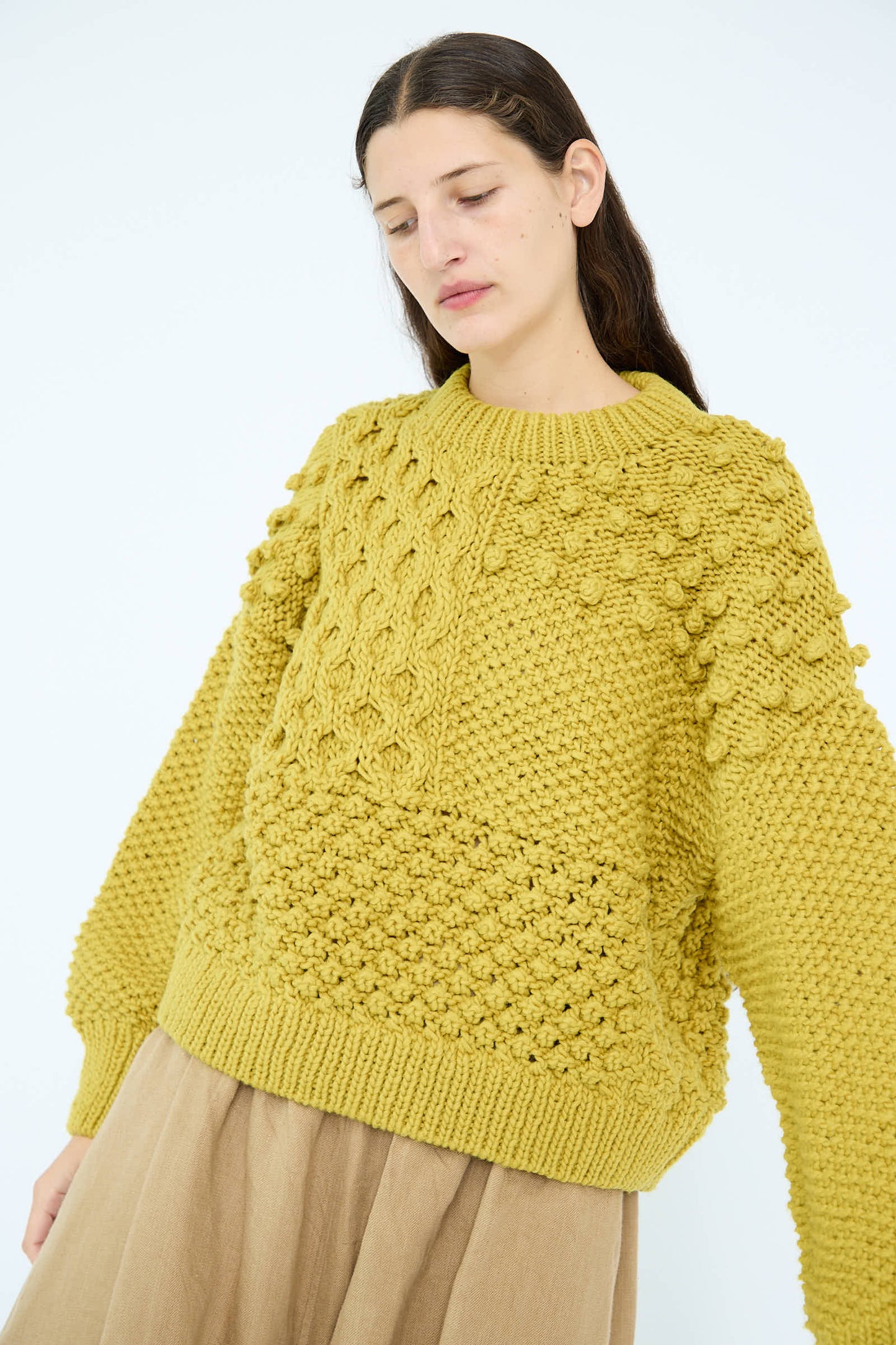 A person modeling the Wool Hand Knit Pullover in Yellow from Ichi Antiquités, fashioned from 100% wool with a striking textured mustard color, stylishly teamed with a beige skirt against a light background.