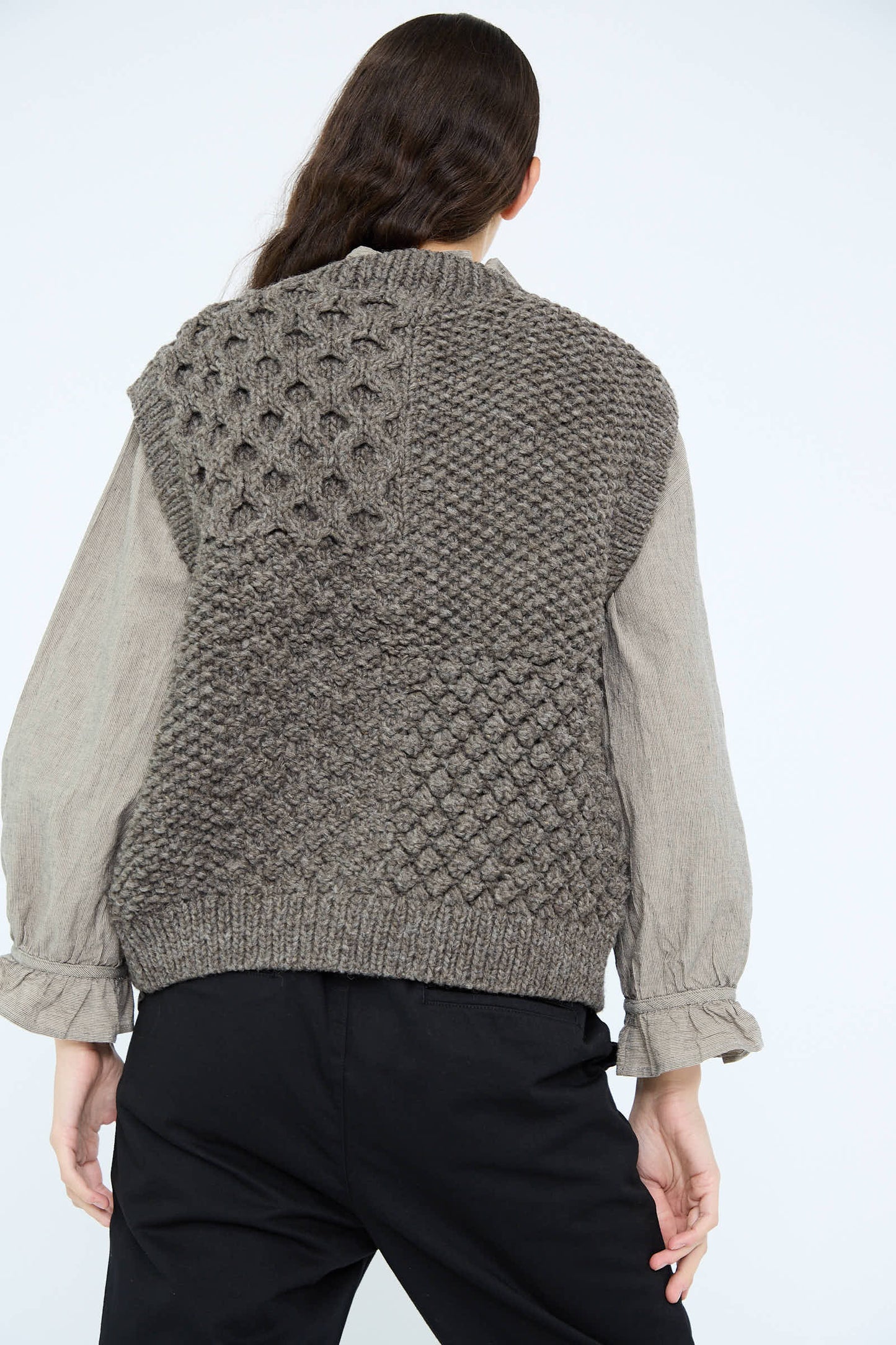 A person with long hair is seen from the back, wearing an Ichi Antiquités Hand Knit Wool Vest in Mocha over a light gray shirt.