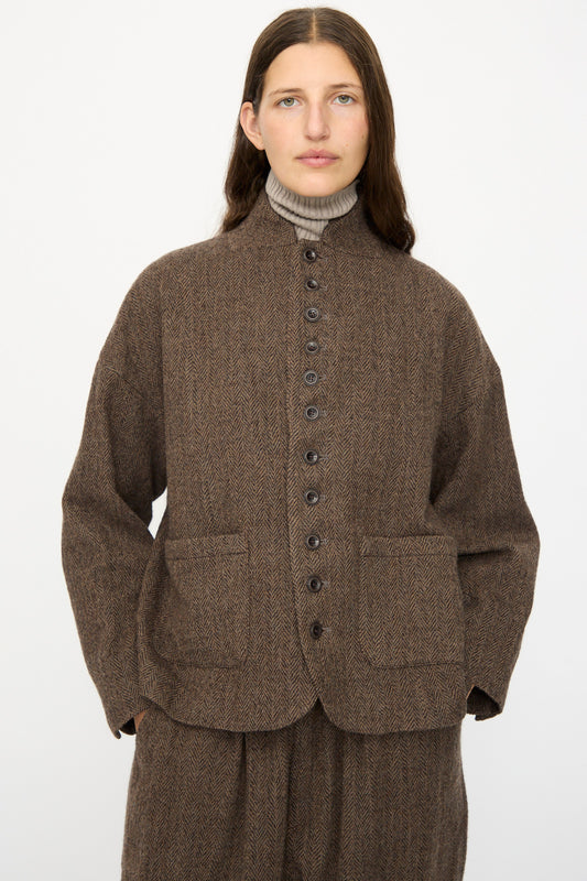 A person with long brown hair wears the Ichi Antiquités Wool Herringbone Jacket in Brown over a beige turtleneck, paired with matching pants, standing against a plain white background.