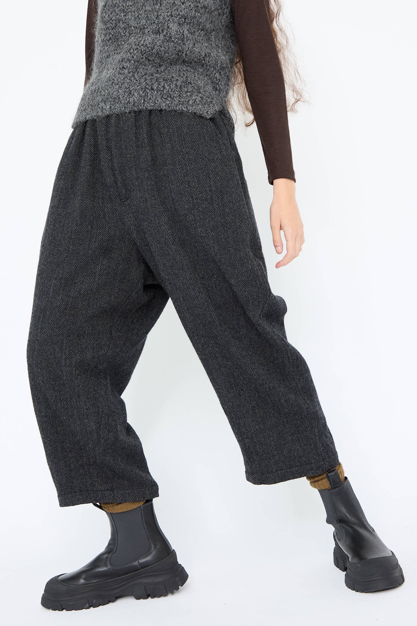 The person is dressed in the Wool Herringbone Pant in Black by Ichi Antiquités, featuring a loose fit and elasticated waist, paired with a dark long-sleeve shirt and stylish black ankle boots.