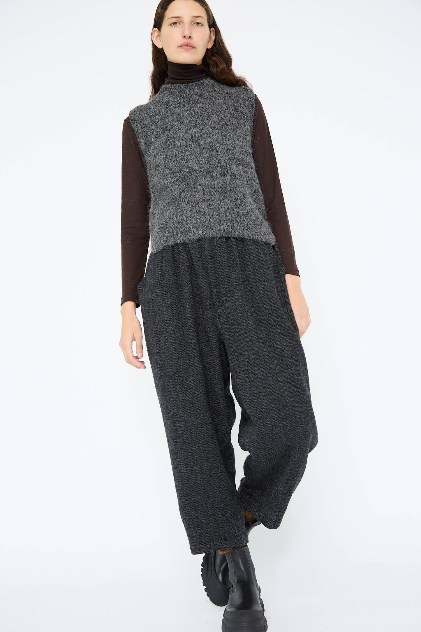 A person wearing a gray sleeveless sweater over a black shirt and wide Wool Herringbone Pant in Black by Ichi Antiquités is standing against a plain background.