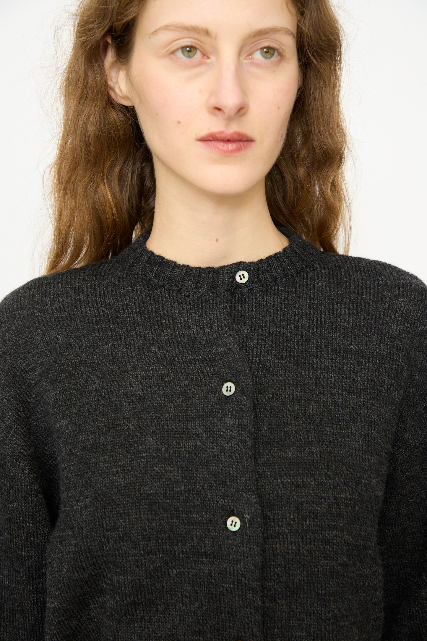 A person with long brown hair wears the Ichi Antiquités Wool Knit Cardigan in Black, made in Japan, and gazes slightly to the side against a plain background.