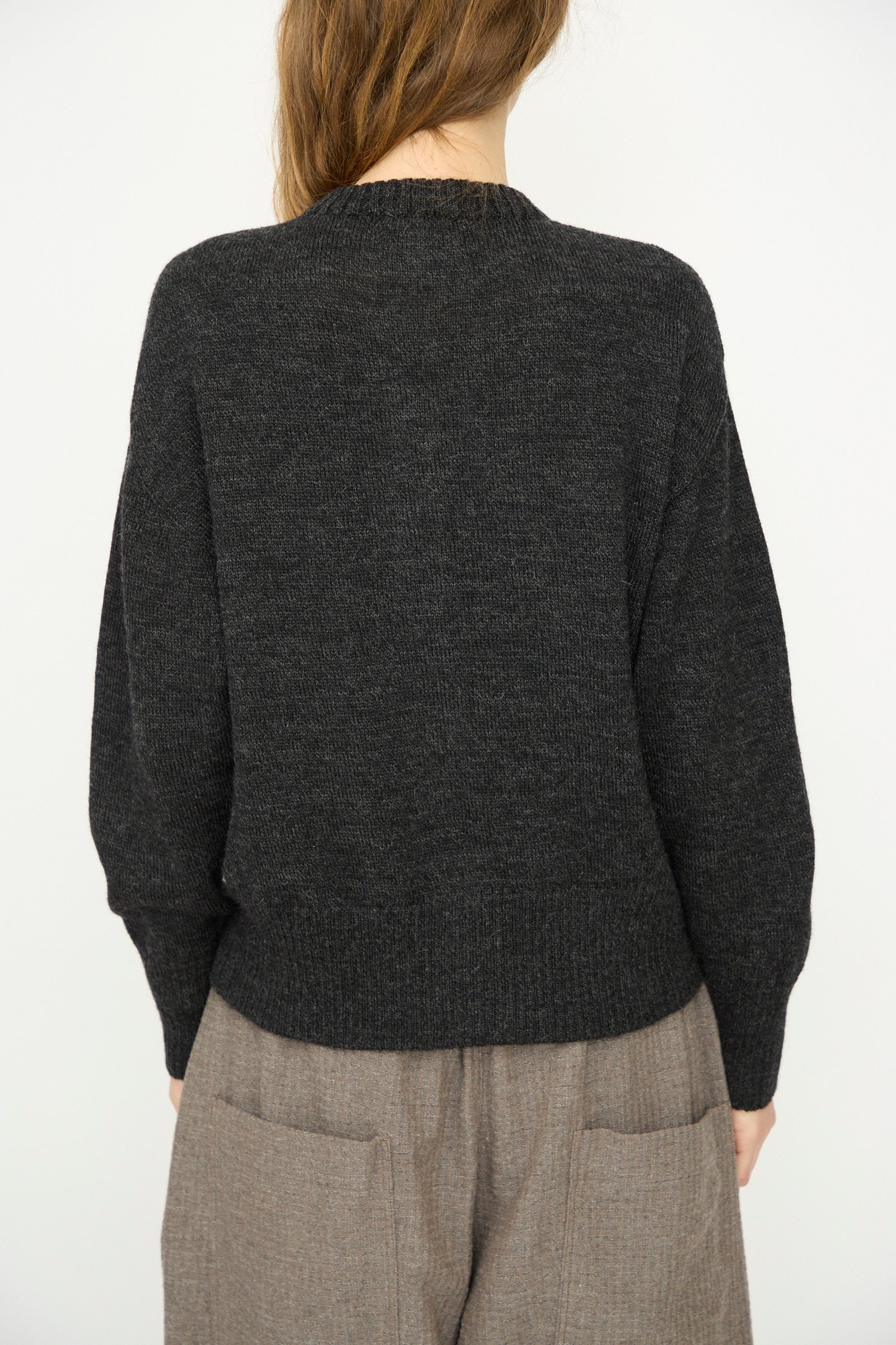 A person faces away from the camera, wearing the Ichi Antiquités Wool Knit Cardigan in Black and loose brown pants, set against a plain light background.
