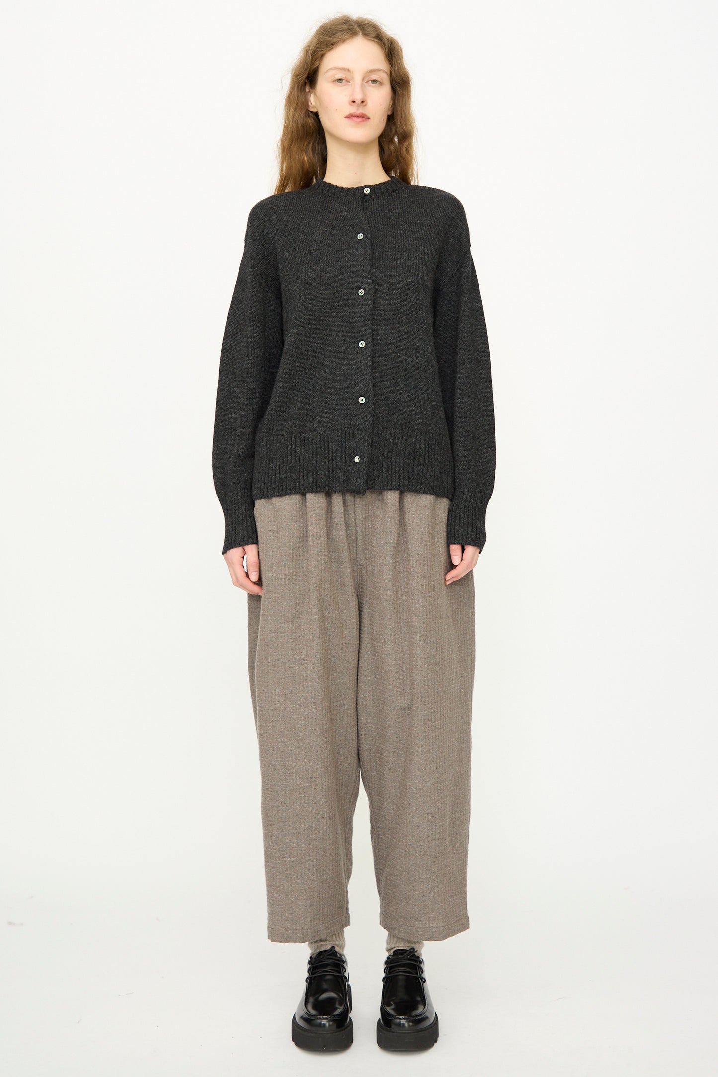 A person faces forward against a plain white background, wearing the Ichi Antiquités Wool Knit Cardigan in Black, paired with loose beige pants and black shoes.