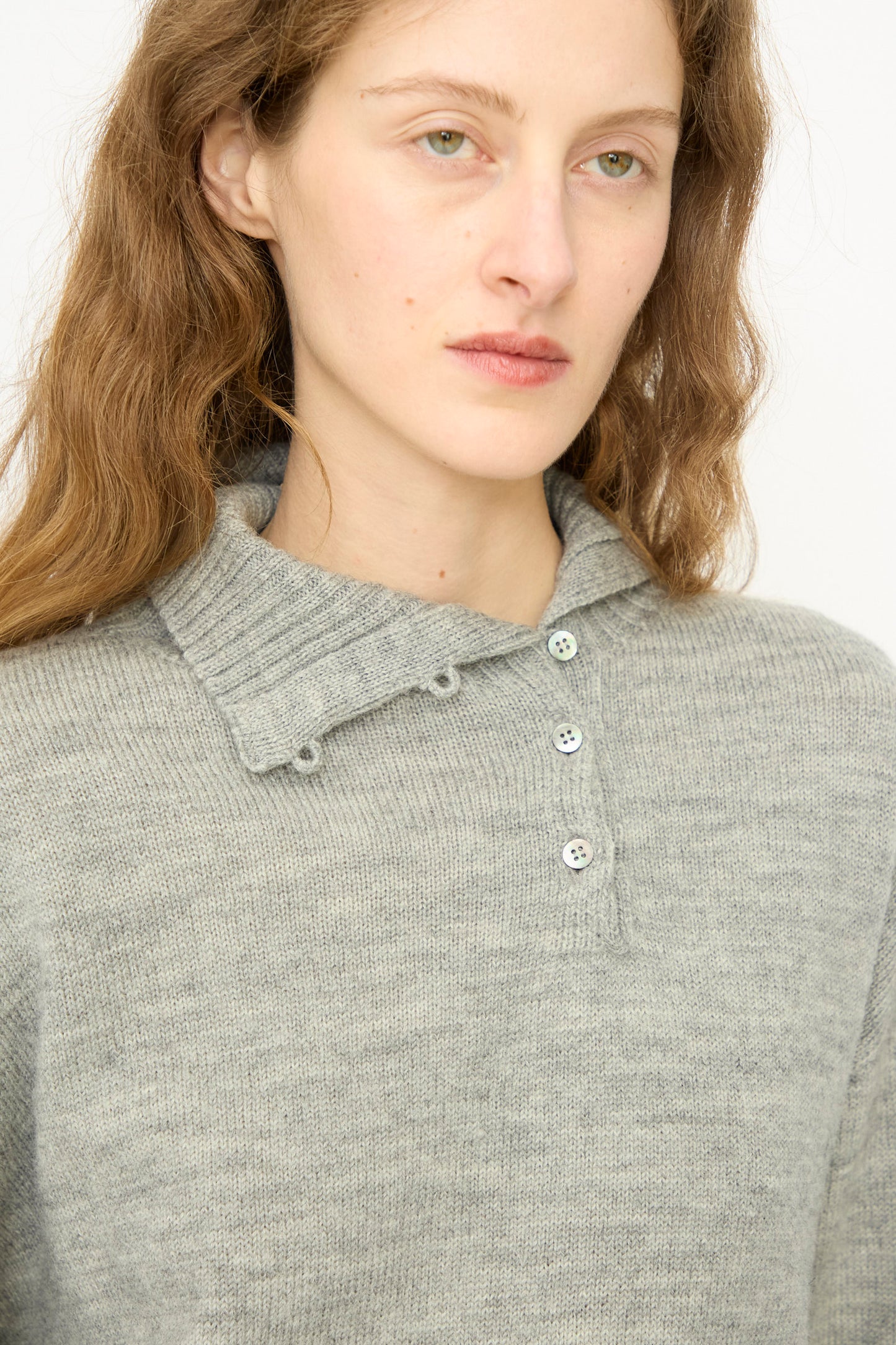 A person with long brown hair wears the Ichi Antiquités Wool Knit Pullover in Gray, featuring a ribbed collar and three buttons, posed slightly to the side against a plain background.