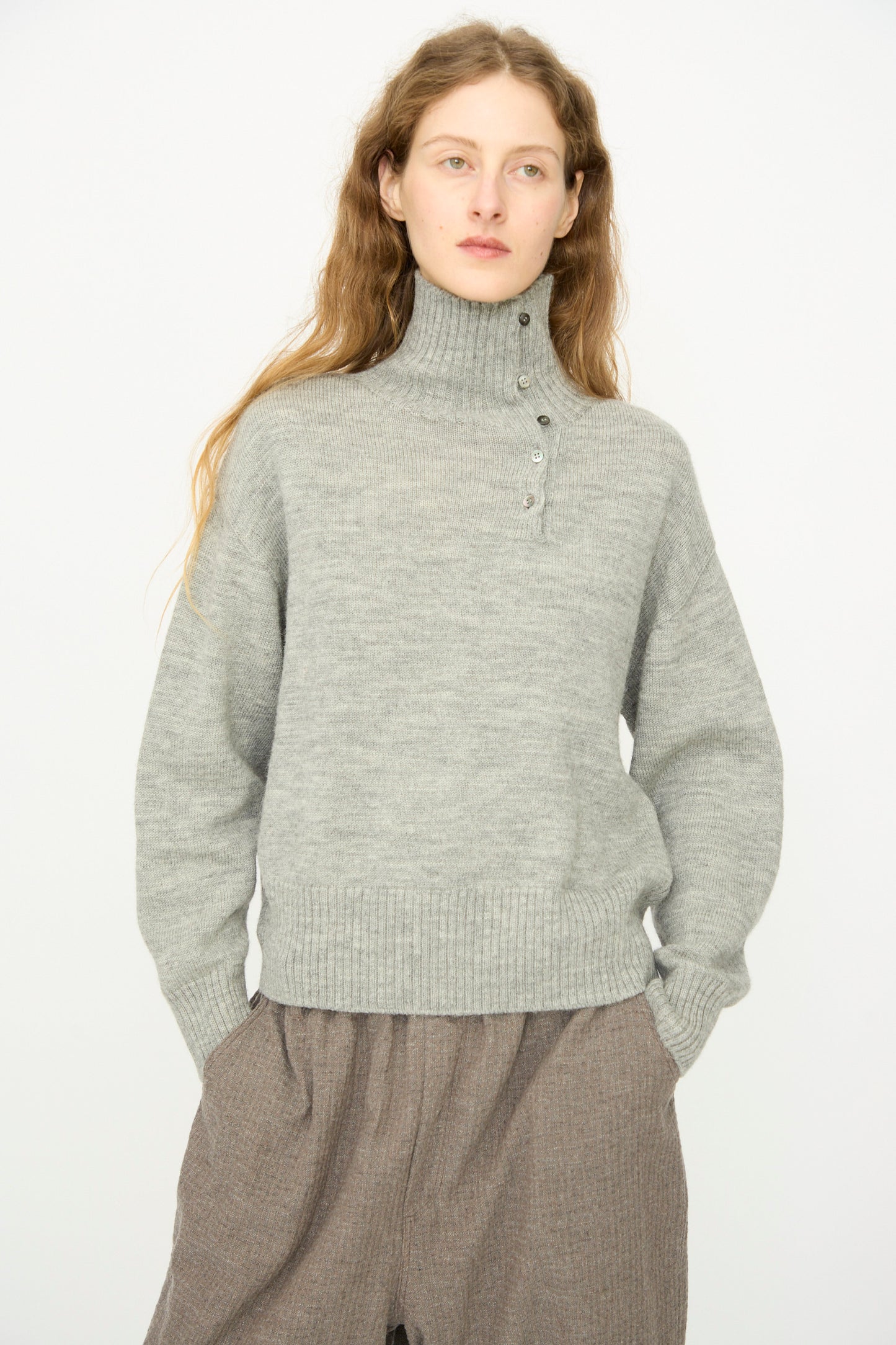 A person with long light brown hair wears the Ichi Antiquités Wool Knit Pullover in Gray, styled with loose brown pants, standing against a plain white background.