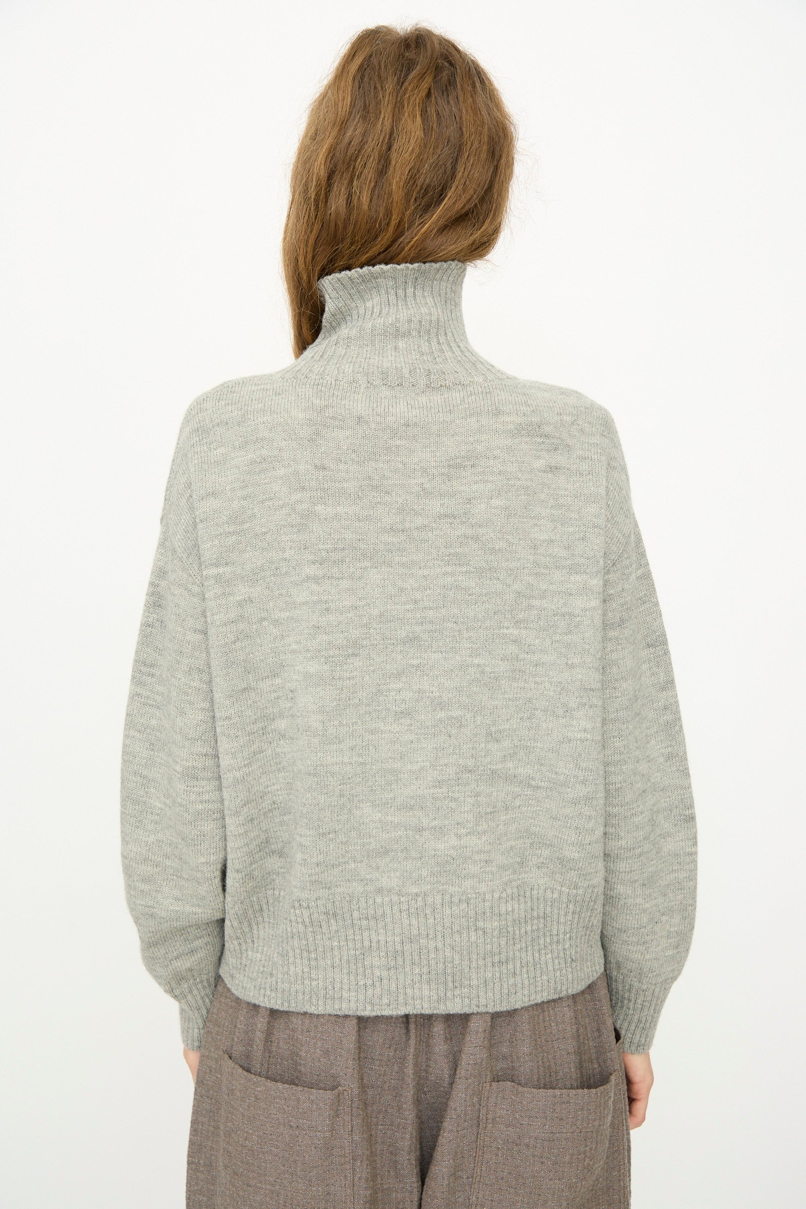 A person faces away from the camera, wearing the Ichi Antiquités Wool Knit Pullover in Gray with brown pants, set against a plain white background.