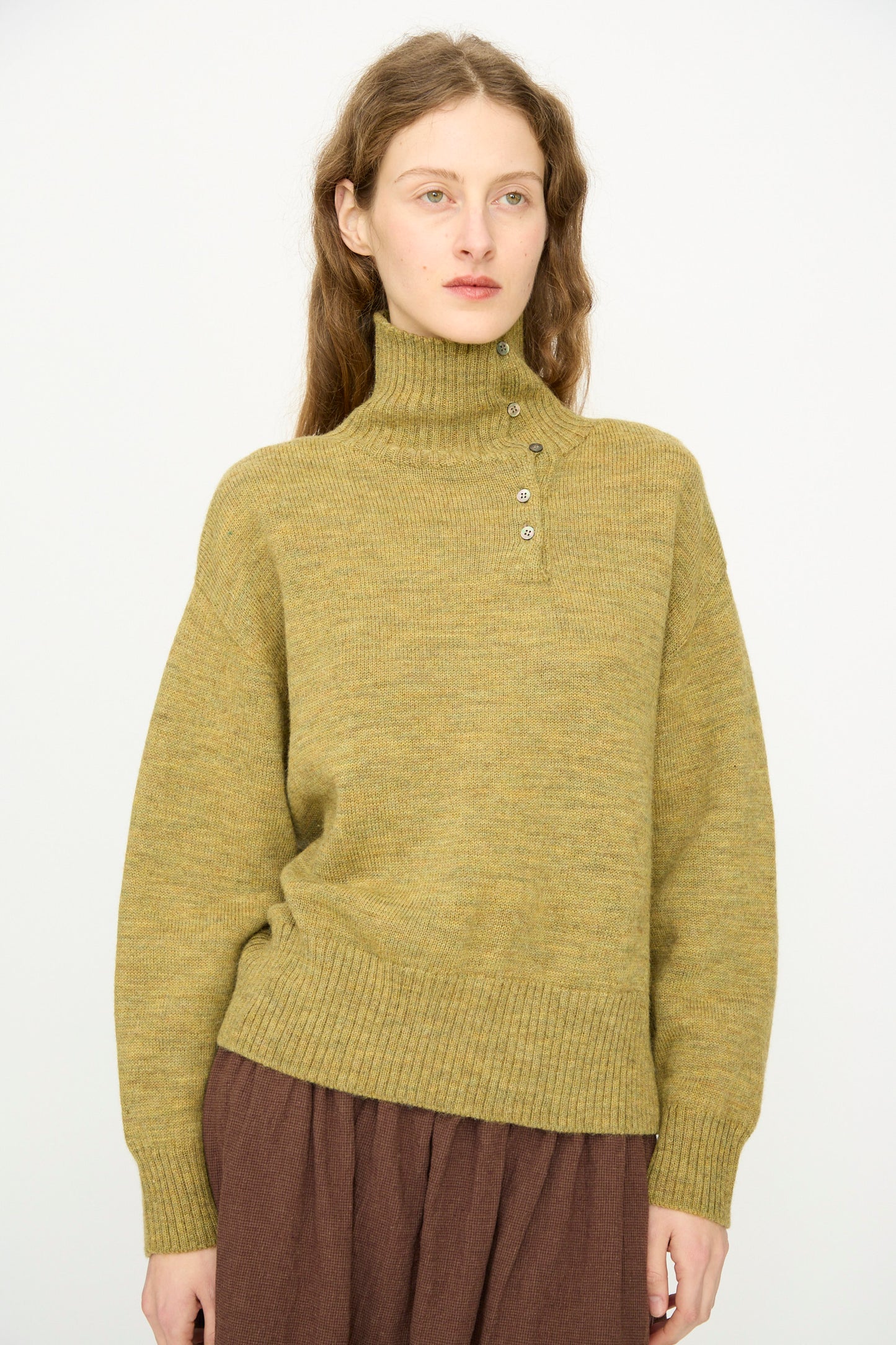 A person with long brown hair wears the Ichi Antiquités Wool Whole Garment Knit Pullover in Mustard and a brown skirt, standing against a plain white background.