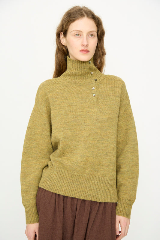 A person with long brown hair wears the Ichi Antiquités Wool Whole Garment Knit Pullover in Mustard and a brown skirt, standing against a plain white background.