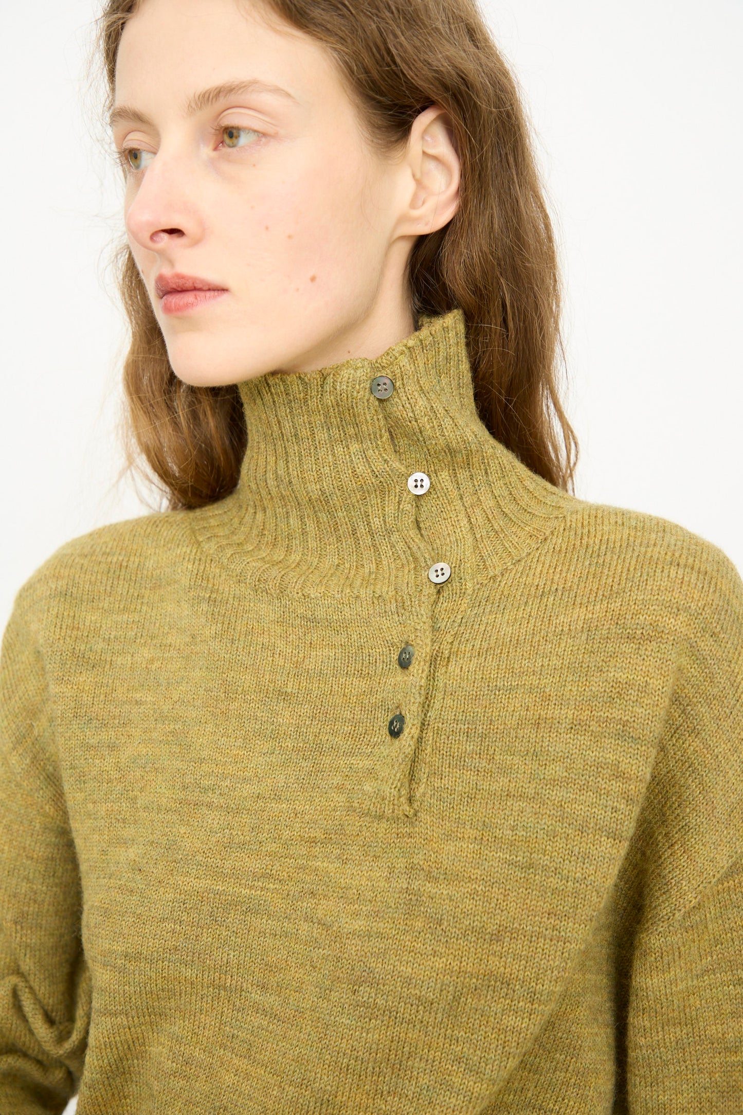 A person wears the Ichi Antiquités Wool Whole Garment Knit Pullover in mustard, featuring a high-neck and ribbed collar, looking to the side against a plain background.