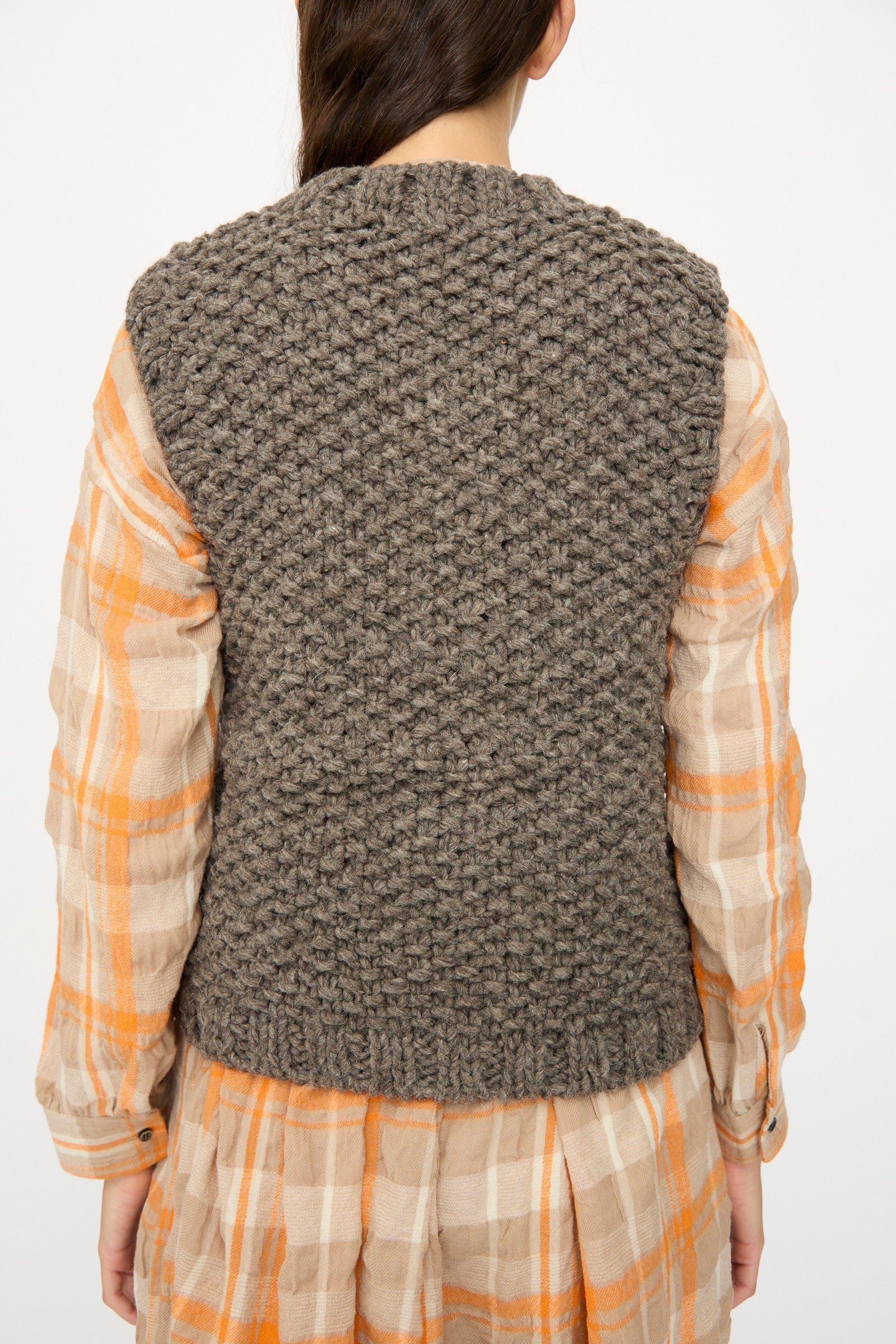 A person wears the Ichi Antiquités Wool Peru Hand-knit Vest in Gray over an orange and beige plaid dress, photographed from the back.
