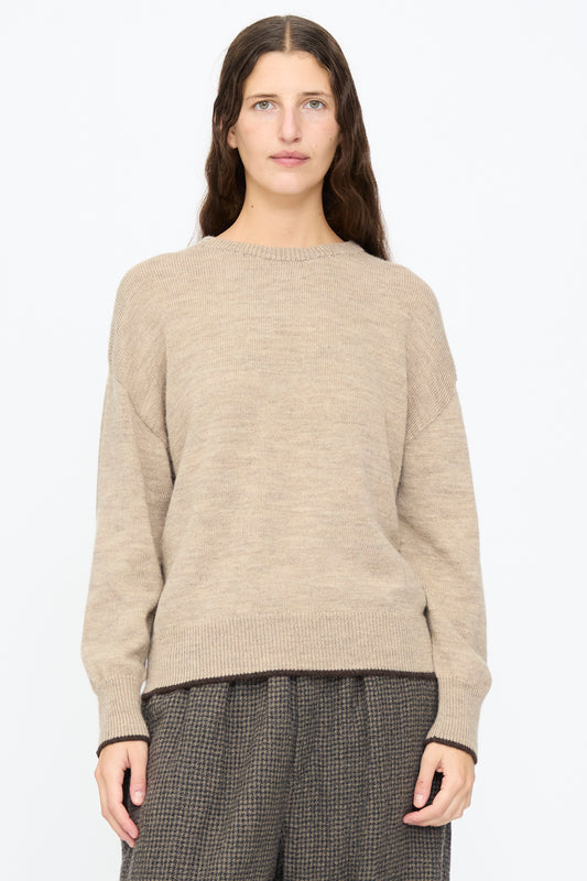 A person wearing an Ichi Antiquités Wool Pullover in Beige and Brown, featuring dark brown trim at the hem and cuffs, paired with dark patterned trousers.
