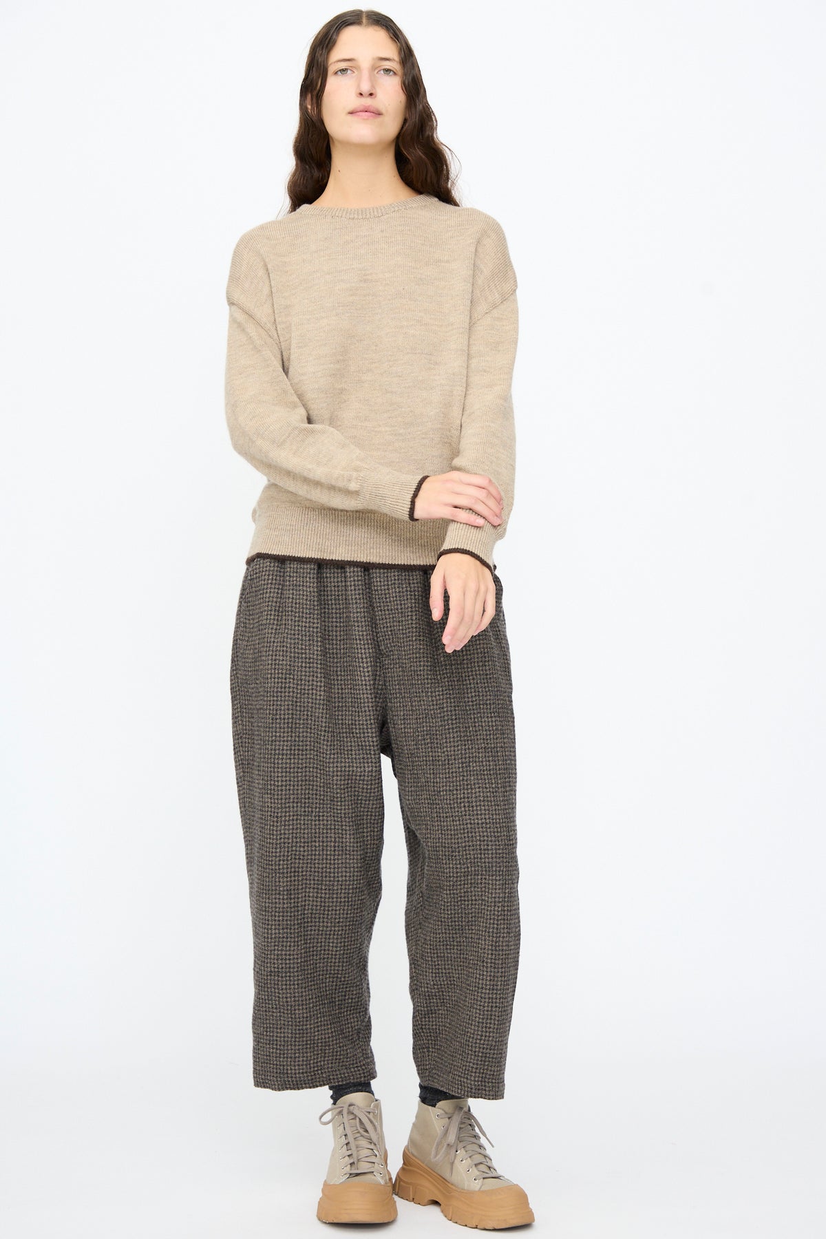 A person wearing an Ichi Antiquités Wool Pullover in Beige and Brown, paired with dark brown patterned trousers and beige platform sneakers.