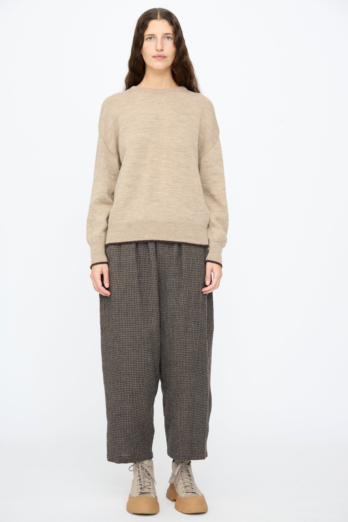 A person wearing an Ichi Antiquités Wool Pullover in Beige and Brown, paired with dark brown patterned trousers and beige lace-up sneakers.