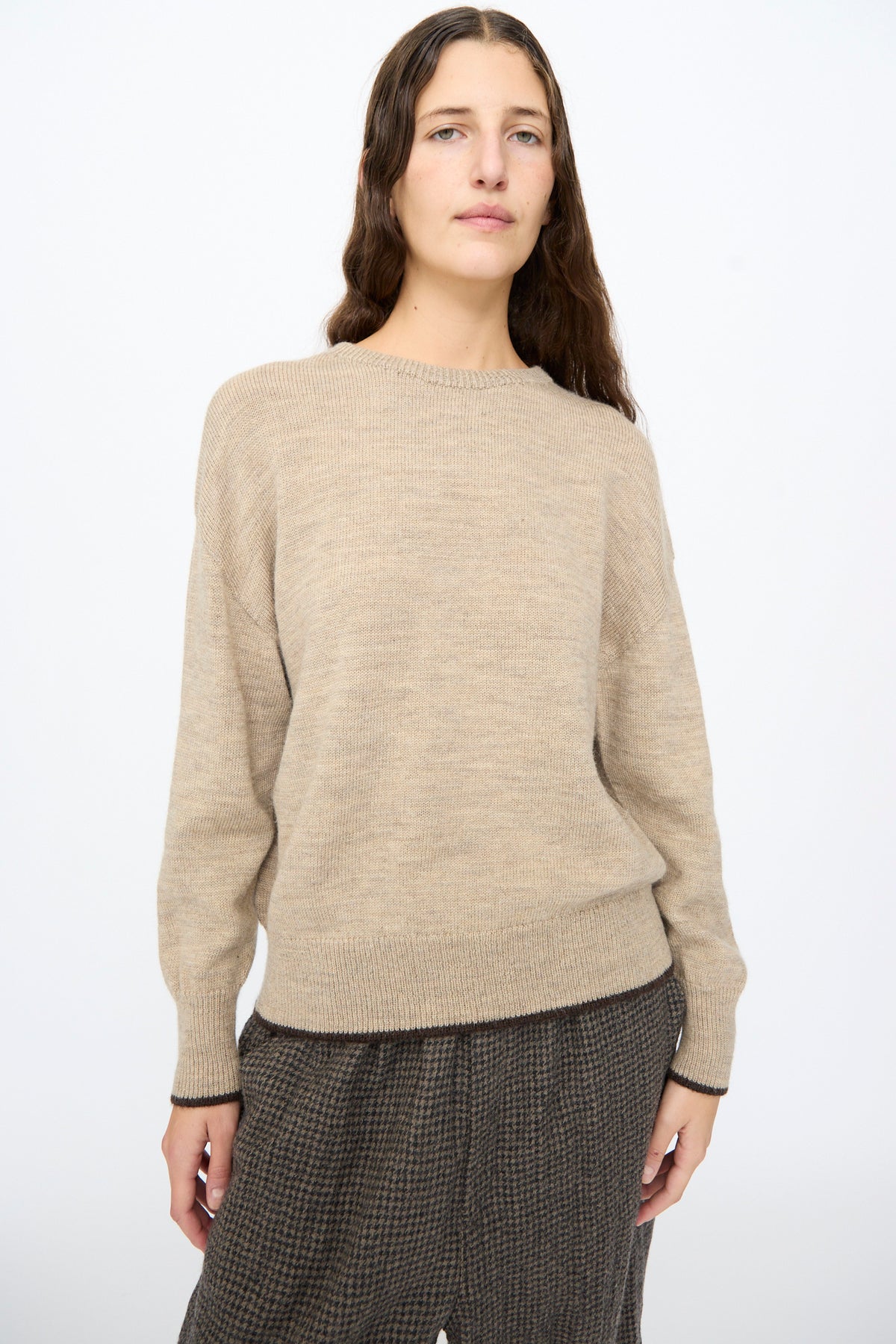 Ichi Antiquités Wool Pullover in beige wool with dark brown trim at the cuffs and hem, worn over dark patterned trousers.