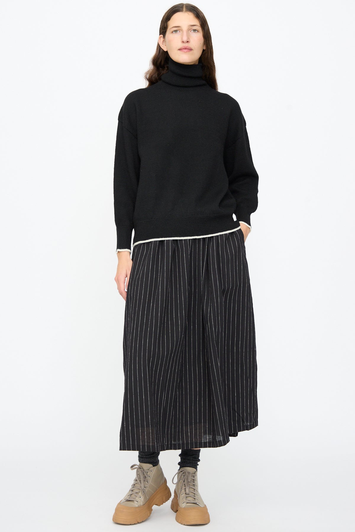 A person wearing an Ichi Antiquités Wool Pullover in Black and White, paired with a black pinstriped midi skirt and tan lace-up platform boots.