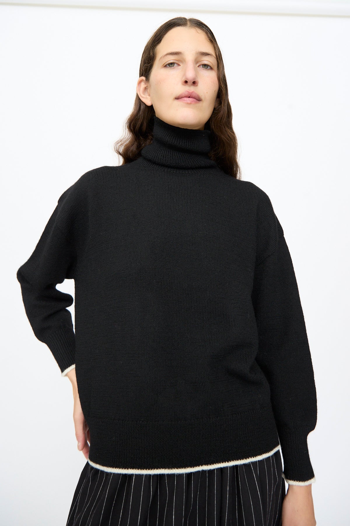A person wearing an Ichi Antiquités Wool Pullover in Black and White, featuring a black wool turtleneck with white trim at the cuffs and hem.