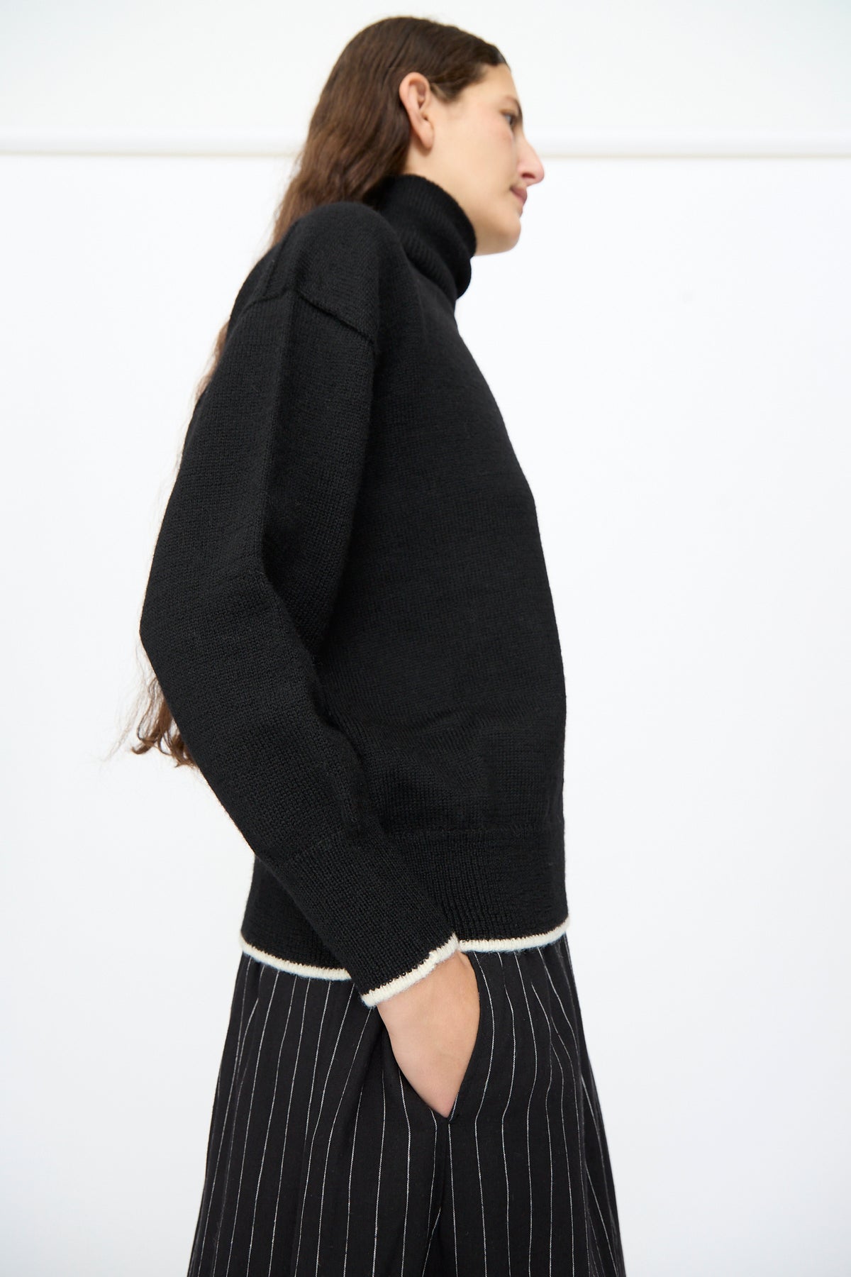 A person wears an Ichi Antiquités Wool Pullover in Black and White, featuring white trim at the cuffs and hem, paired with black pinstripe trousers.