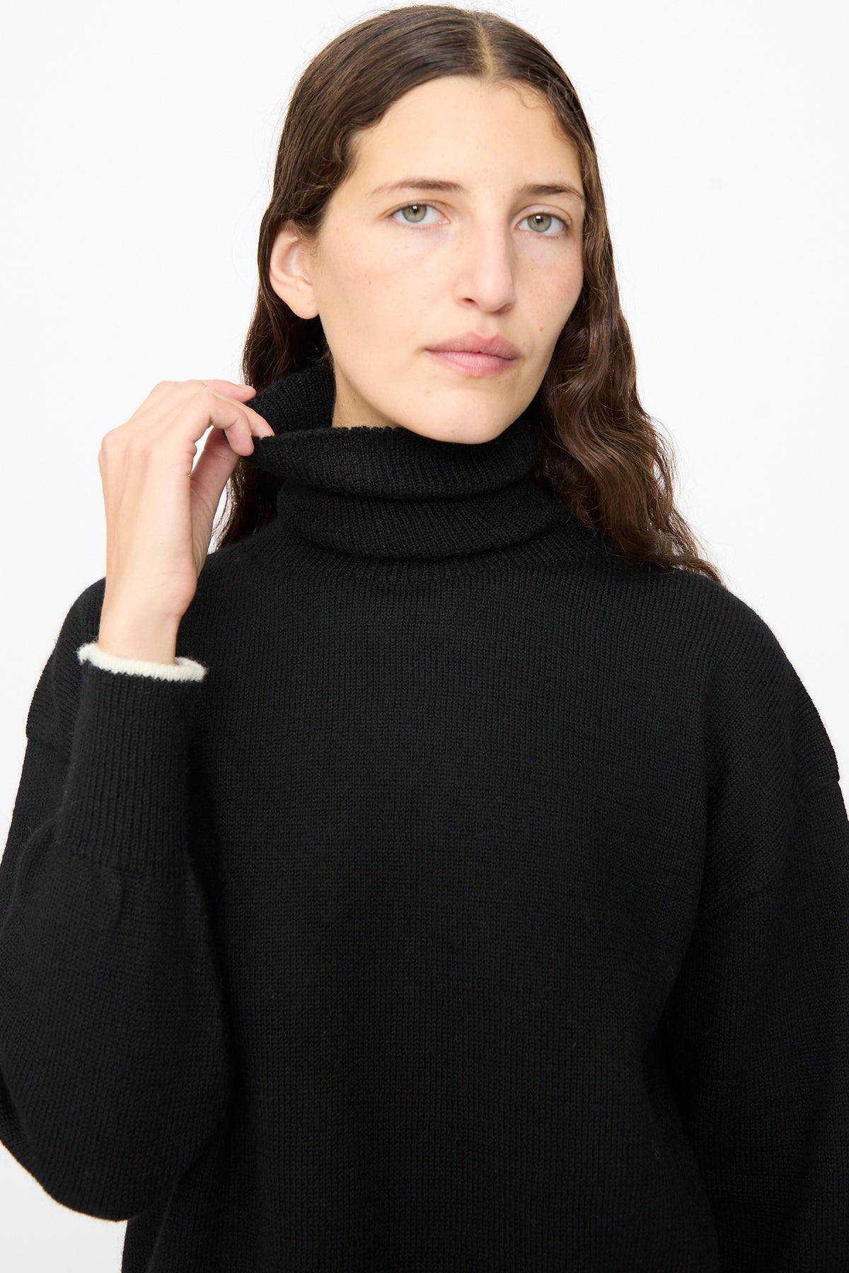 A person wears an Ichi Antiquités Wool Pullover in Black and White, featuring a black wool turtleneck with white trim at the cuffs.