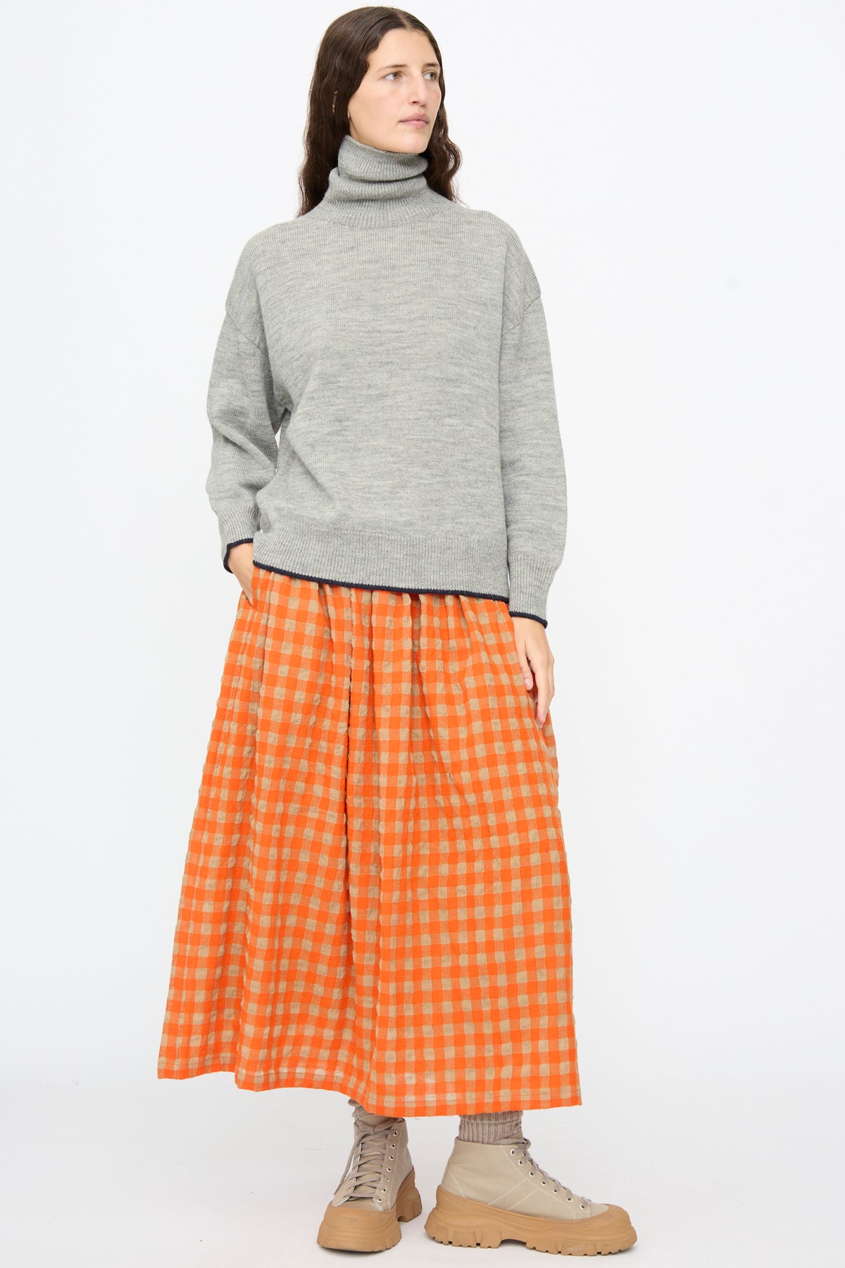 A person wears an Ichi Antiquités Wool Pullover in Gray and Navy with a long orange gingham skirt and beige lace-up boots.