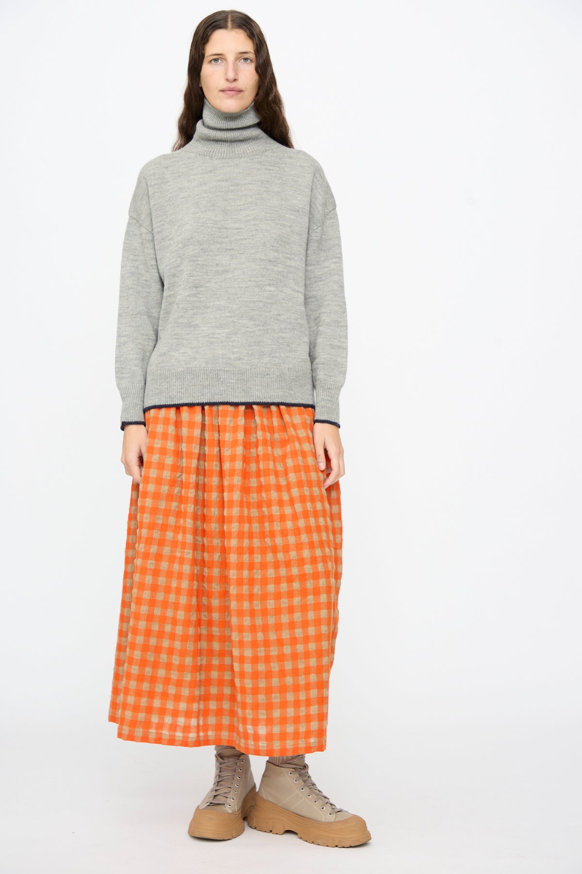 A person wearing an Ichi Antiquités Wool Pullover in Gray and Navy, an orange and tan gingham midi skirt, and tan lace-up platform boots.