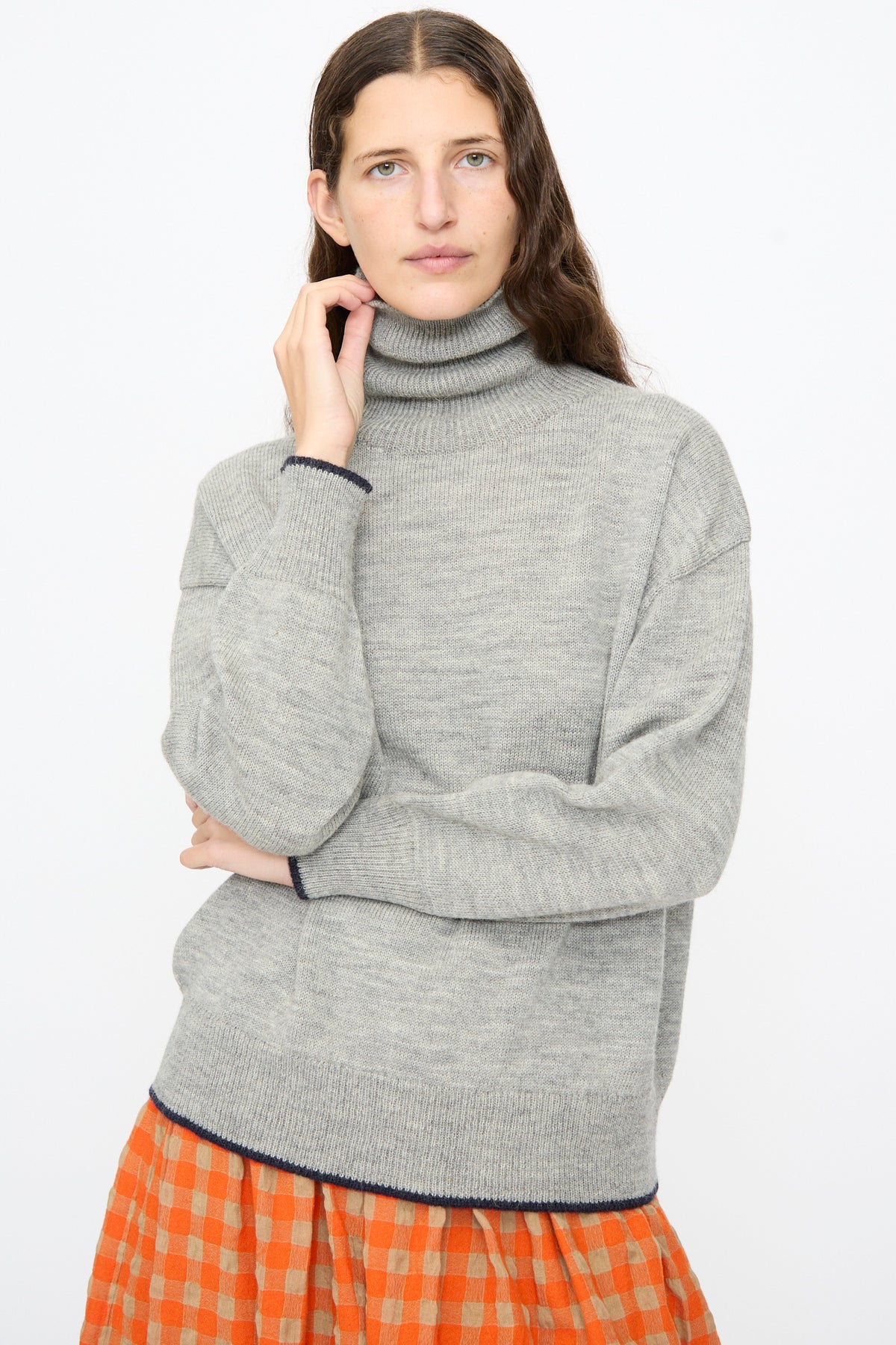 A model wears an Ichi Antiquités Wool Pullover in Gray and Navy with navy trim on the cuffs and hem, paired with an orange and beige checkered skirt.