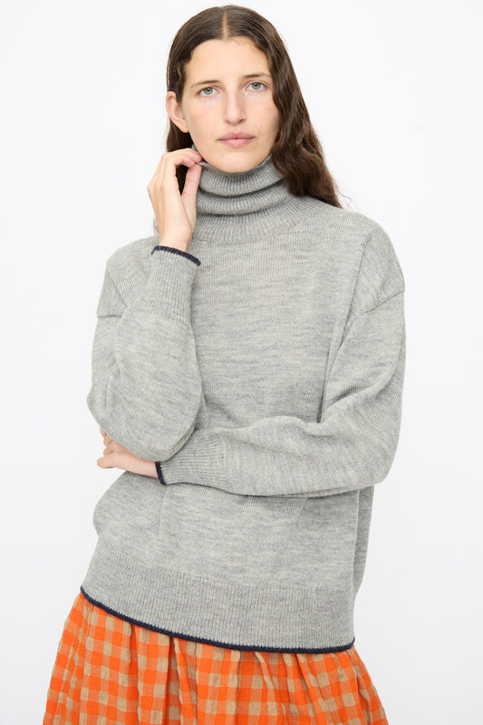A model wears an Ichi Antiquités Wool Pullover in Gray and Navy with navy trim on the cuffs and hem, paired with an orange and beige checkered skirt.