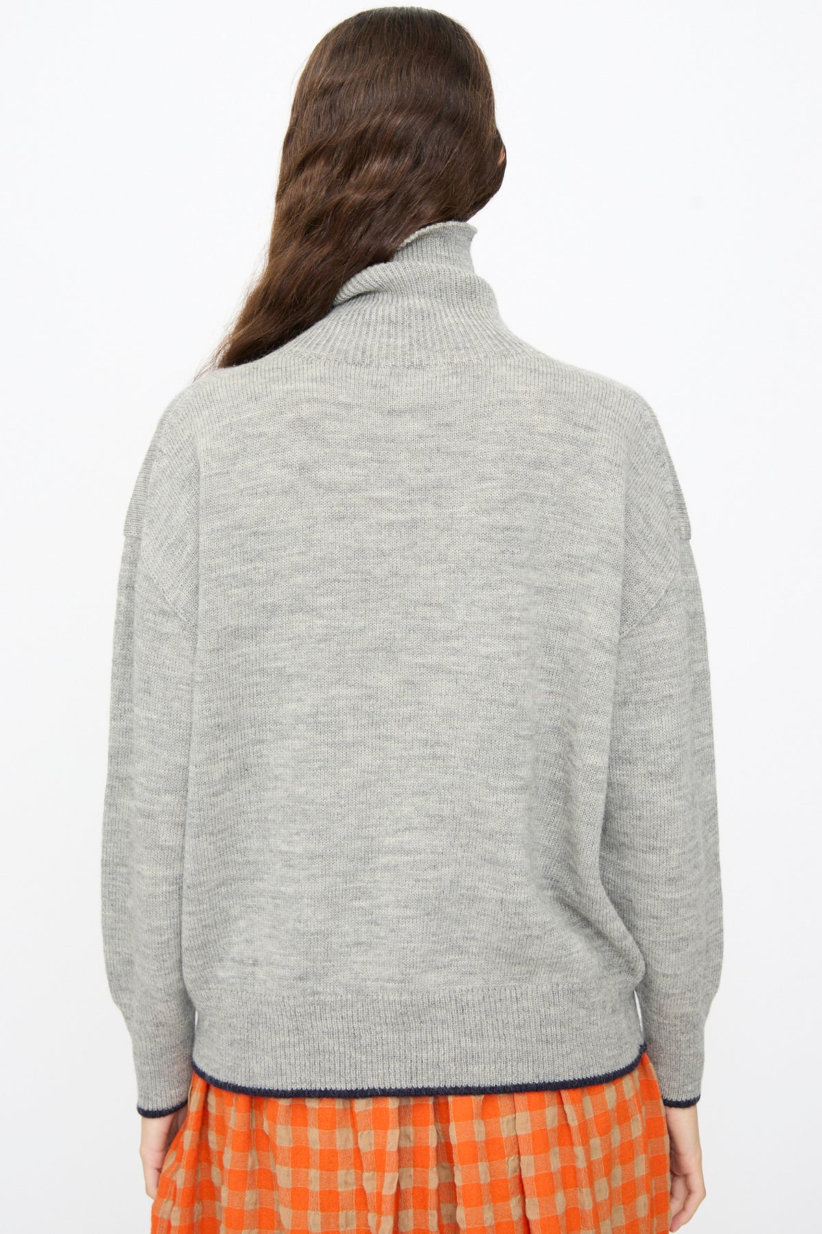 A person wearing an Ichi Antiquités Wool Pullover in Gray and Navy, a gray wool turtleneck sweater with a thin navy trim at the hem.