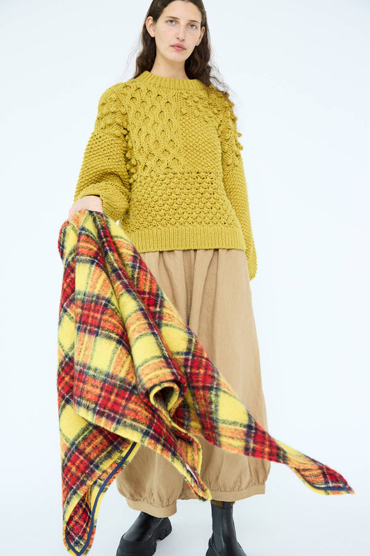 A person wearing a yellow knit sweater and tan pants holds the Ichi Antiquités Wool Tartan Shaggy Stole in Yellow, showcasing its versatility for any occasion.