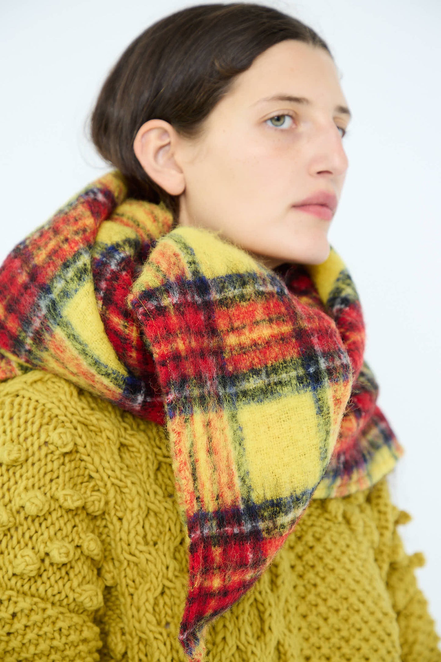 A person with dark hair dons a chunky sweater and the Wool Tartan Shaggy Stole in Yellow by Ichi Antiquités, seamlessly merging style and warmth.