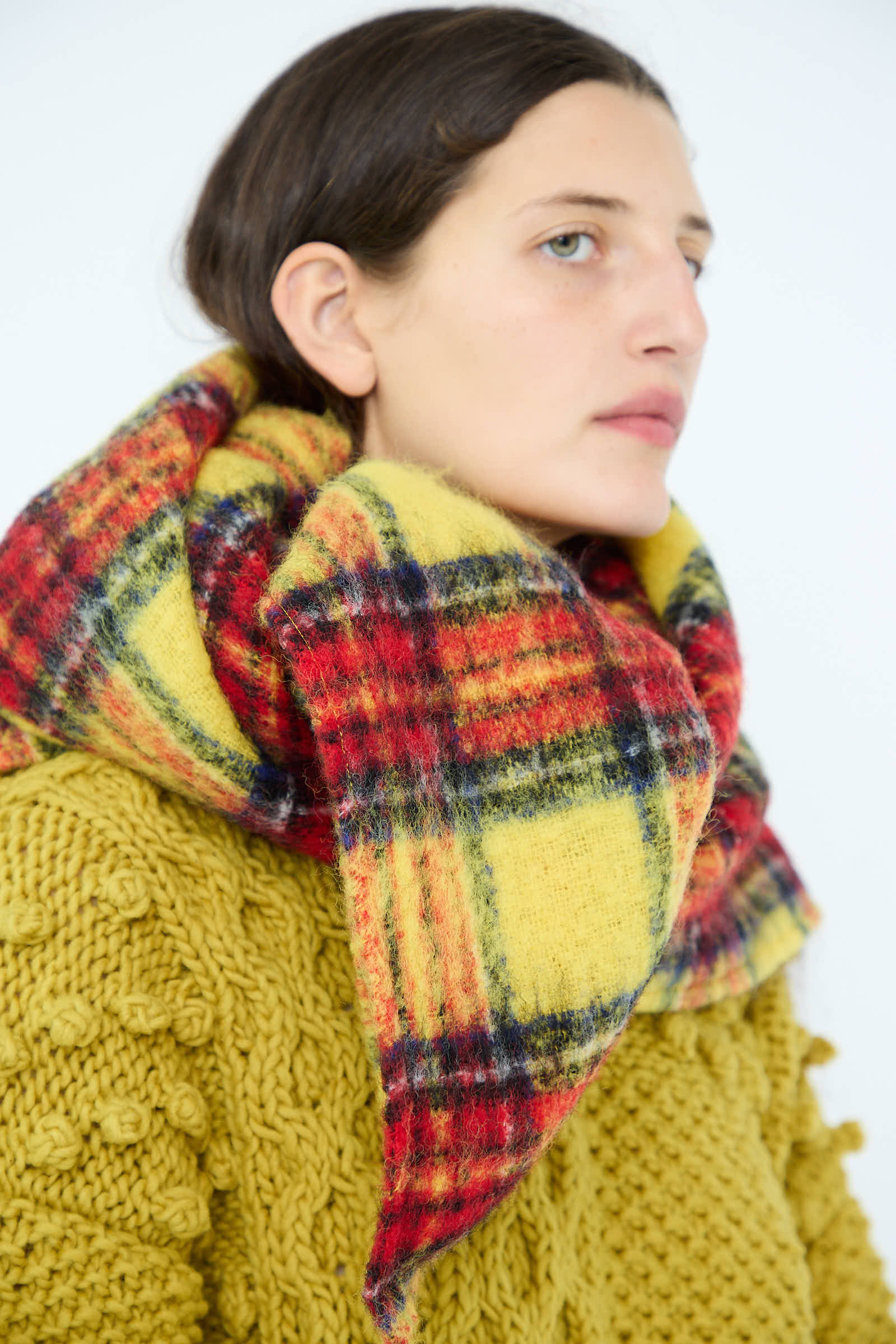 A person with dark hair dons a chunky sweater and the Wool Tartan Shaggy Stole in Yellow by Ichi Antiquités, seamlessly merging style and warmth.