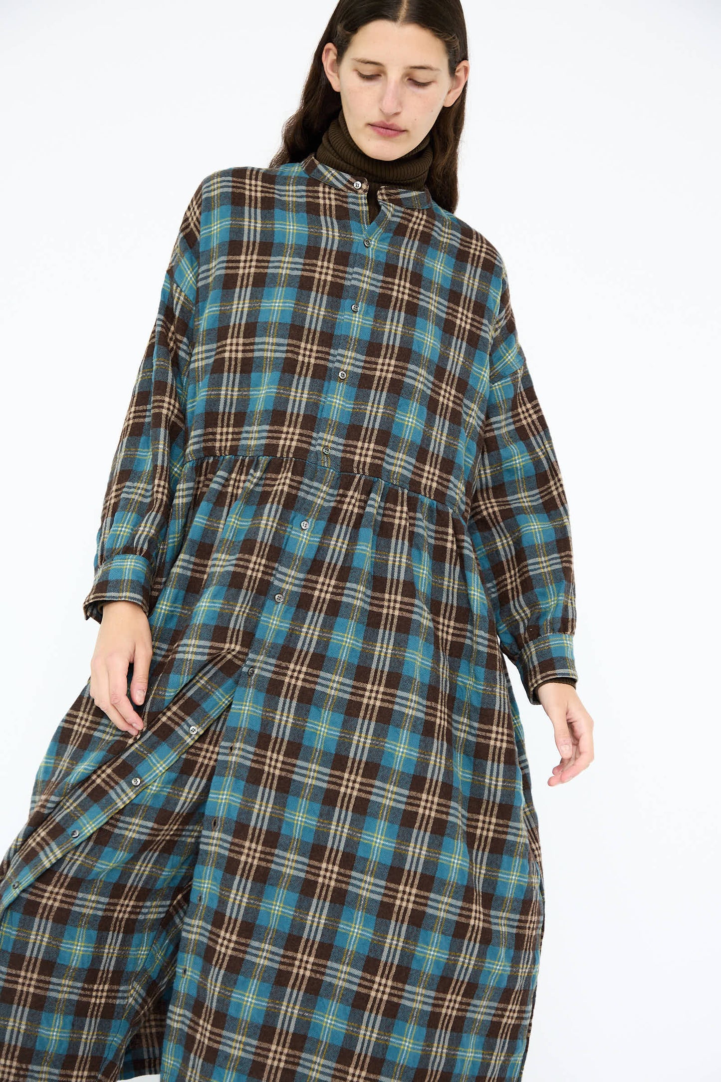 A person wearing the Ichi Antiquités Wool and Cotton Washer Tartan Dress in Blue, featuring a relaxed fit and high collar, stands against a plain white background.