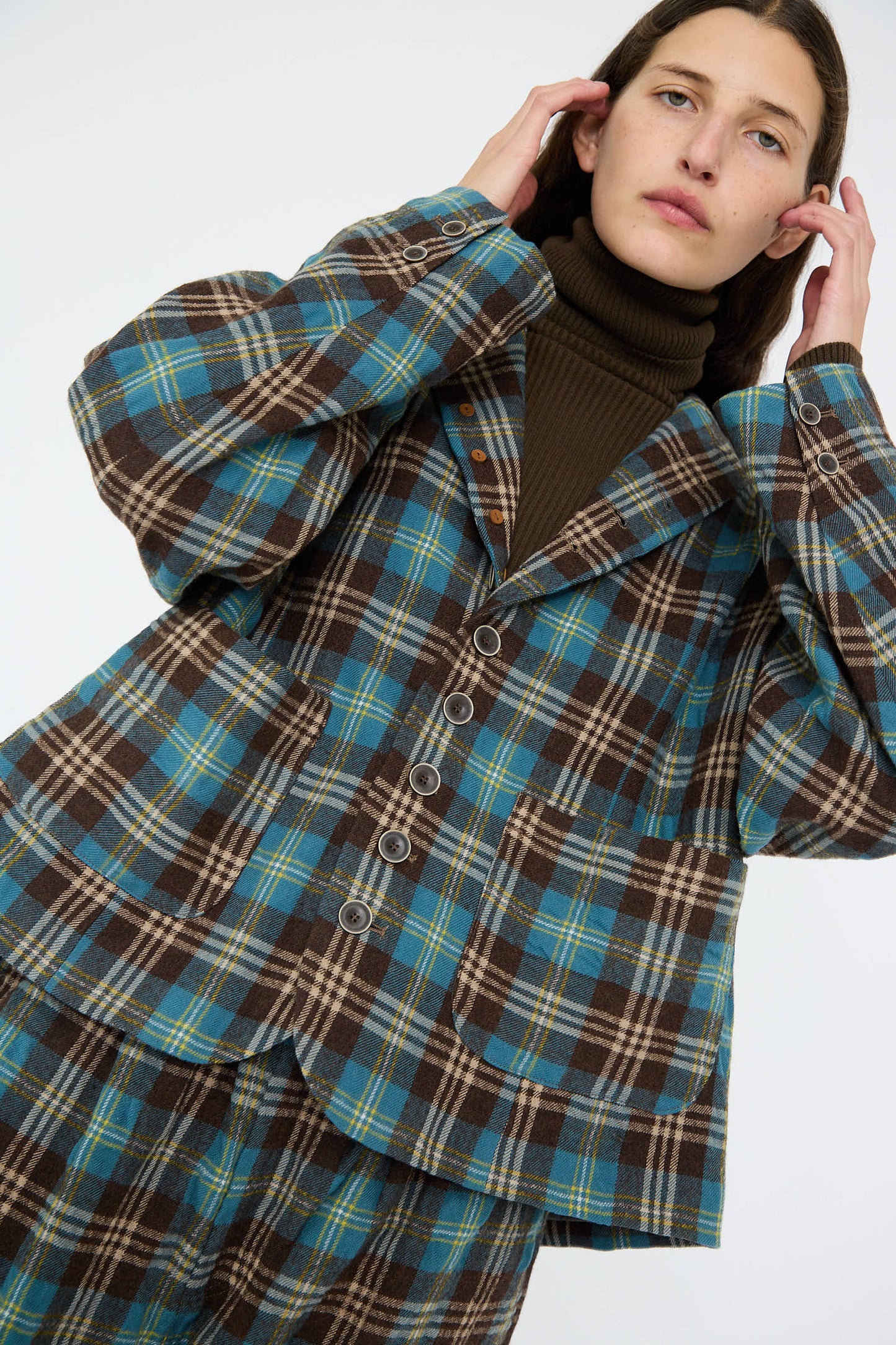 Dressed in a Wool Washer Tartan Jacket in Blue by Ichi Antiquités, a person adjusts their hair against a plain background. The plaid outfit, with its relaxed fit and notched collar blazer design, features shades of brown and blue.