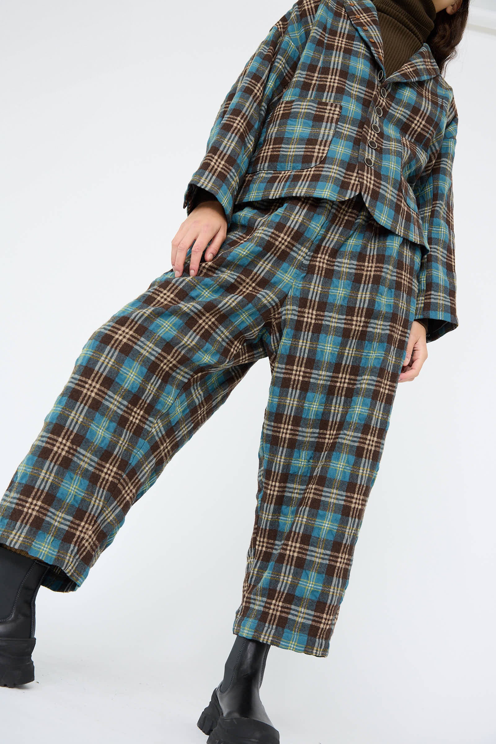 An individual wearing the Wool Washer Tartan Pant in Blue by Ichi Antiquités, paired with black boots and photographed from a low angle.