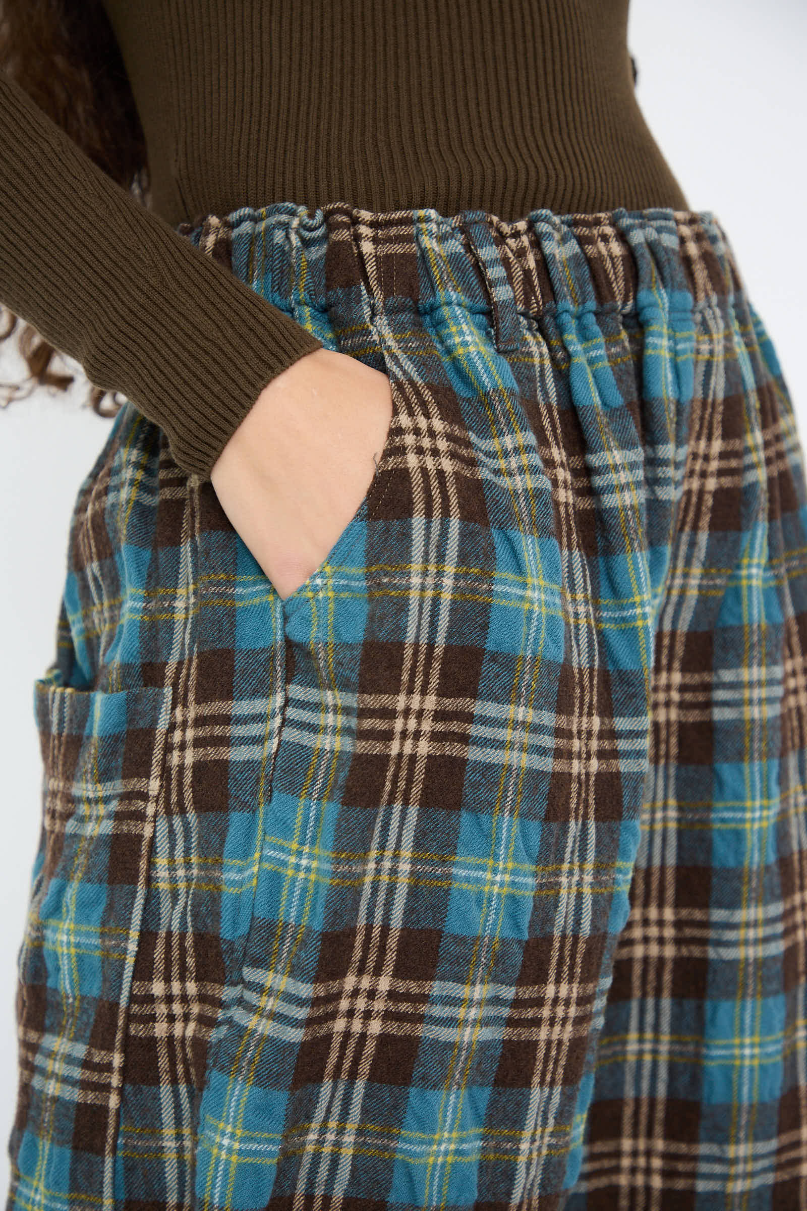 A person dressed in the Wool Washer Tartan Pant in Blue by Ichi Antiquités and a brown ribbed top, with one hand casually placed in their pocket.