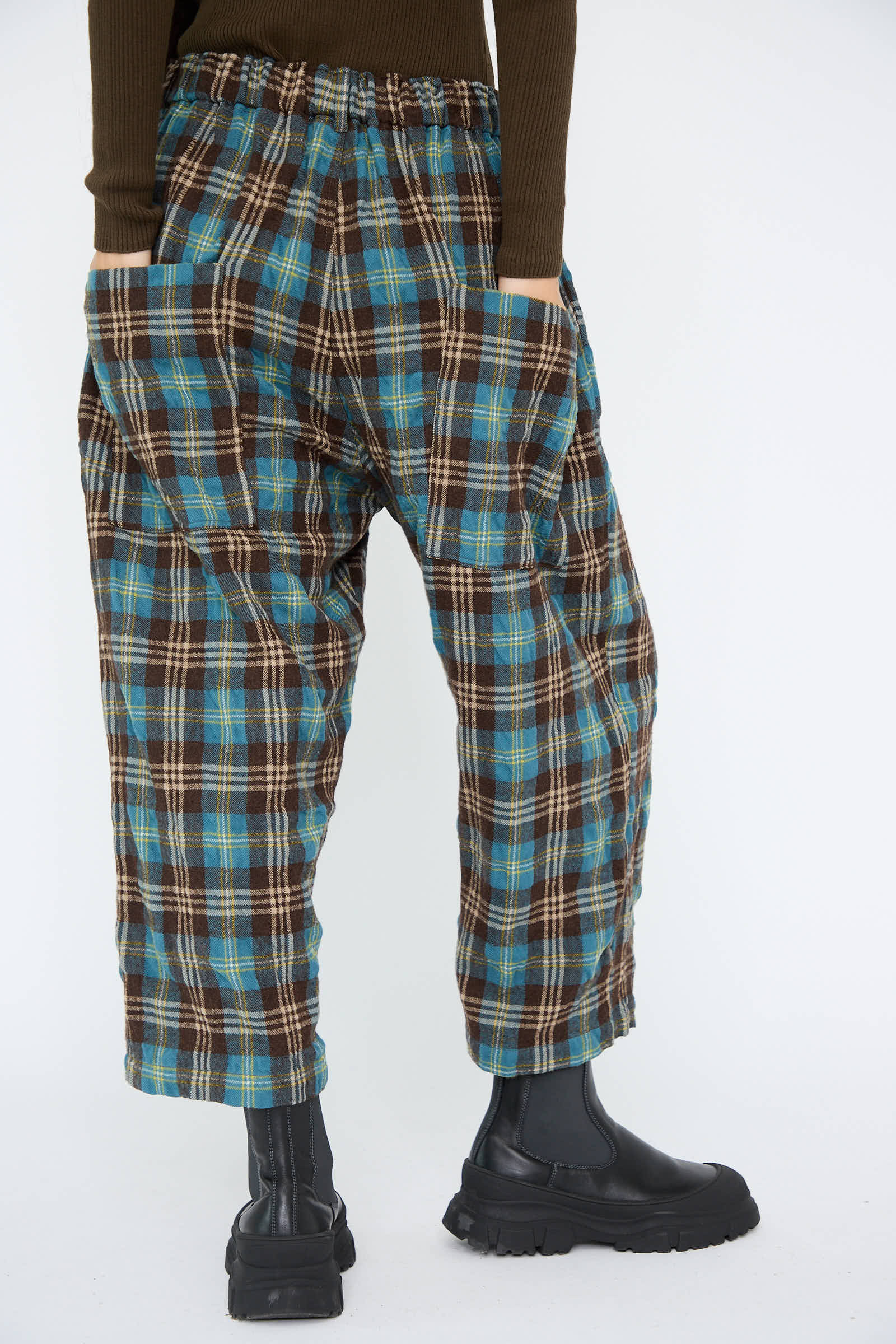 A person is seen from the rear wearing Wool Washer Tartan Pants in Blue by Ichi Antiquités, with their hands in pockets and paired with black boots.