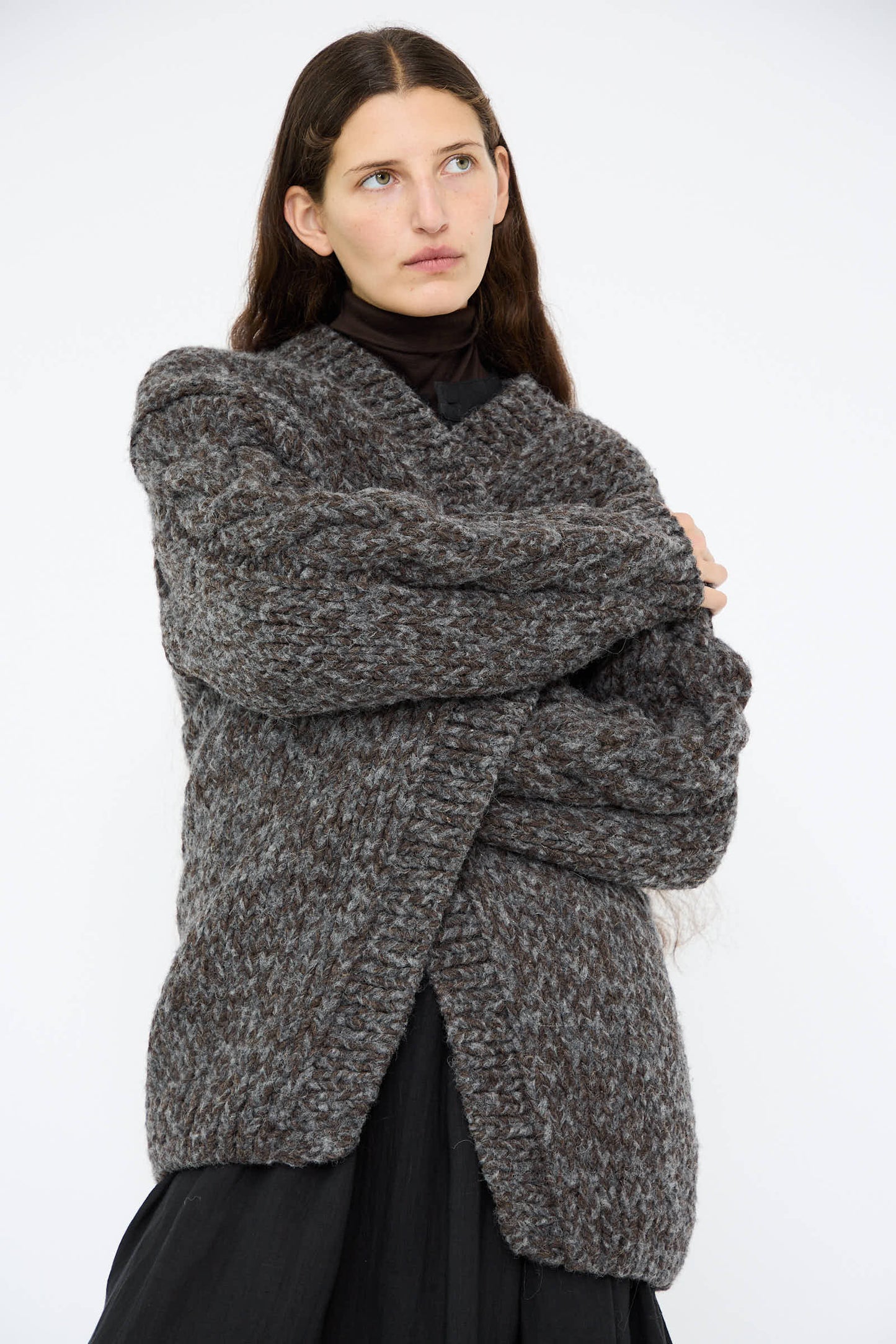 A person with long dark hair is wearing the Wool and Alpaca Hand Knit Cardigan in Charcoal by Ichi Antiquités over a black shirt, standing against a plain white background.