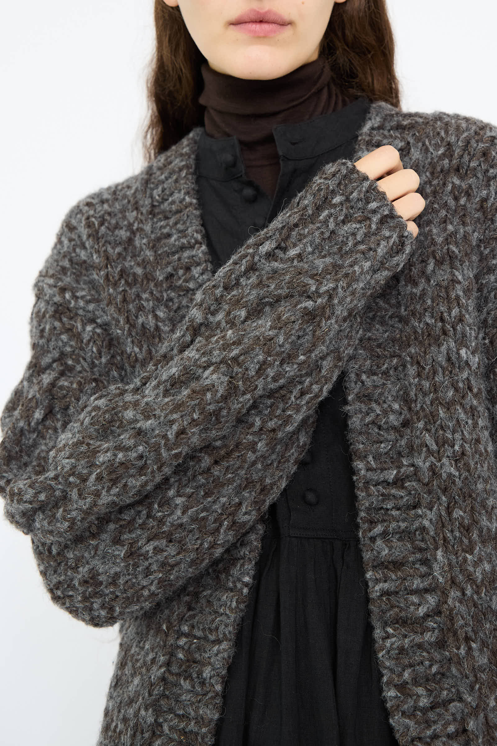 A person in a dark button-up shirt is wearing an open Wool and Alpaca Hand Knit Cardigan in Charcoal by Ichi Antiquités, made of thick, textured knit.