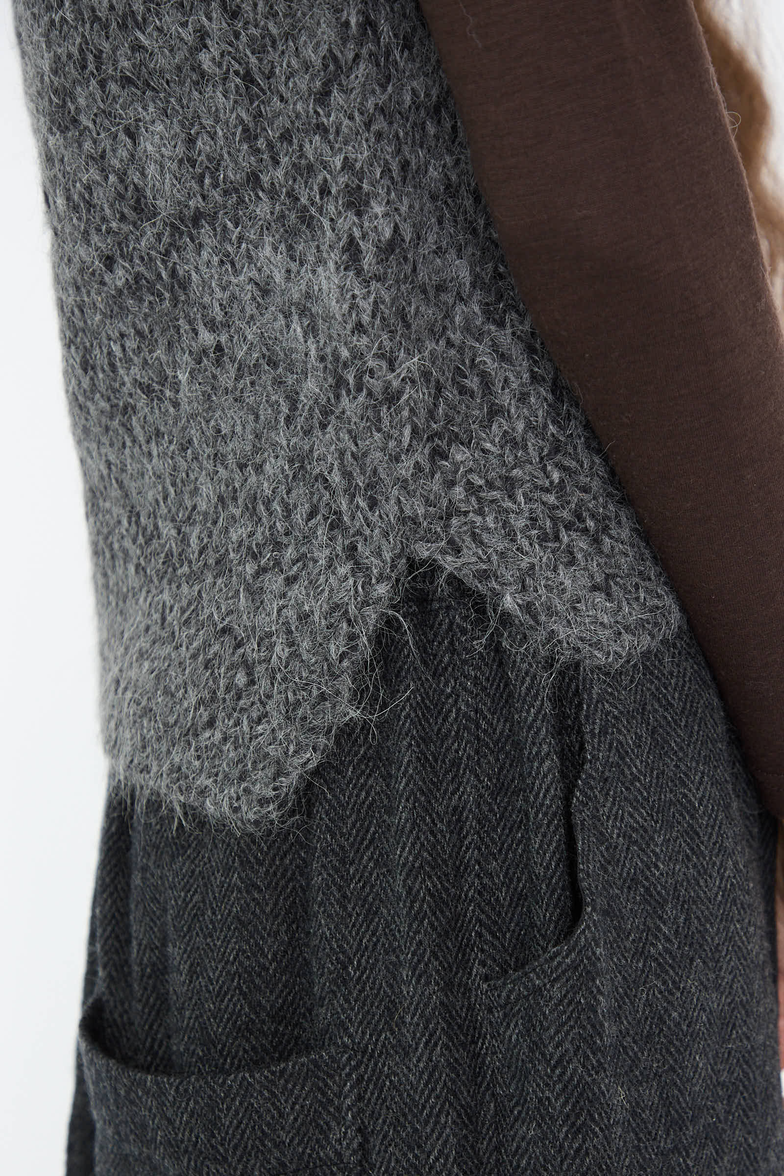 Close-up of layered clothing showcasing the Ichi Antiquités Hand Knit Wool and Alpaca Vest in Gray, designed in a relaxed fit over a darker herringbone-patterned fabric with pockets.