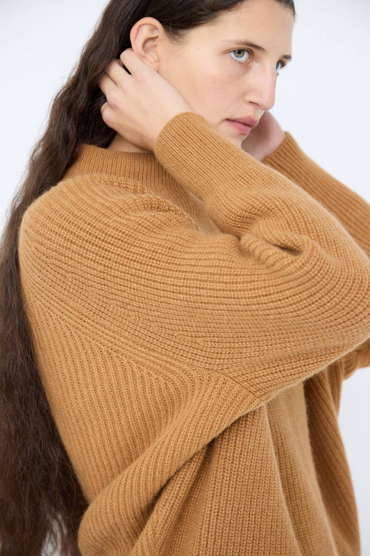 A person clad in the Wool and Angora Ridge Knitted Pullover in Camel by Ichi Antiquités, adjusting their hair with both hands while gazing to the side.