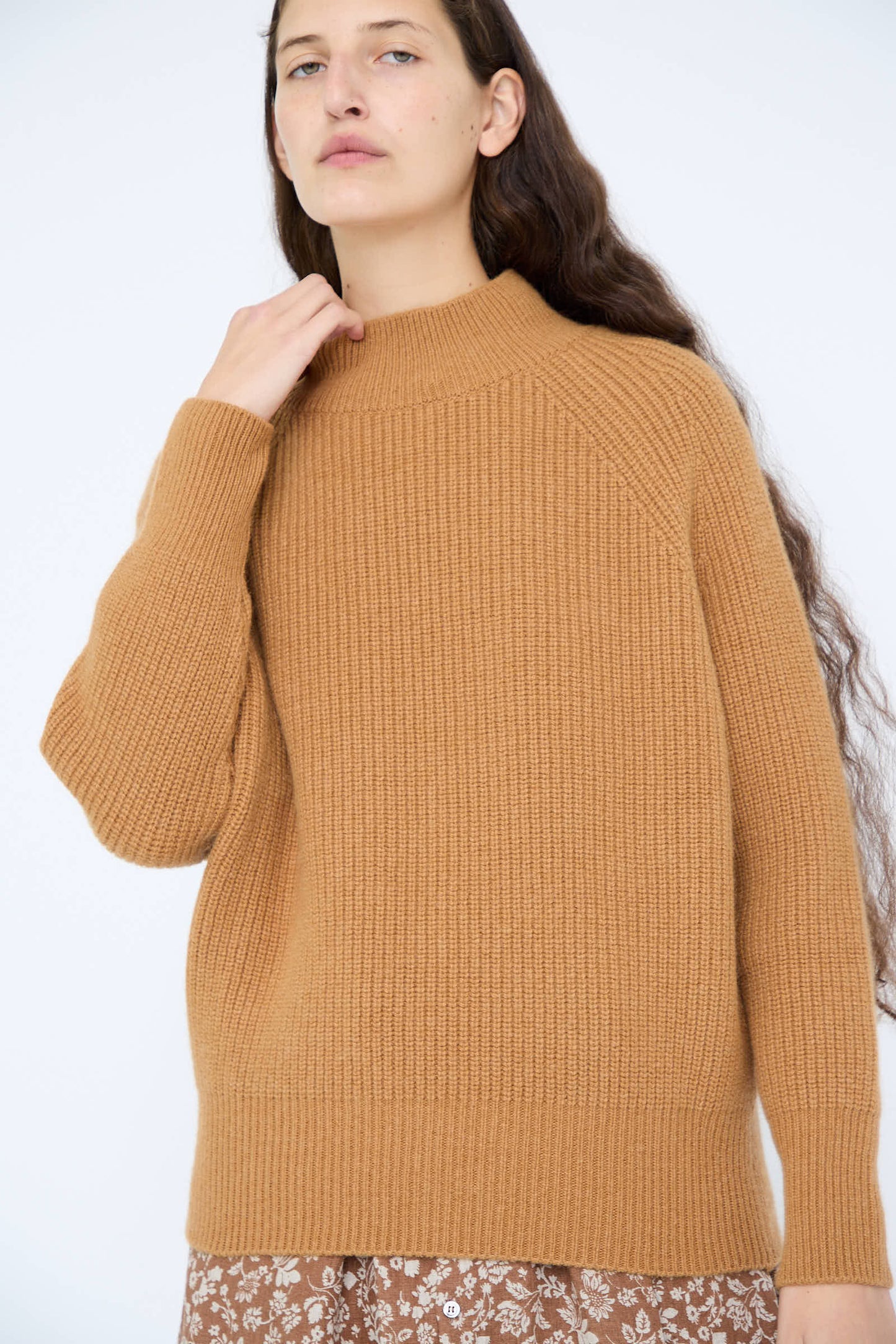 A person wearing the Wool and Angora Ridge Knitted Pullover in Camel by Ichi Antiquités over a floral skirt, standing in front of a plain background.