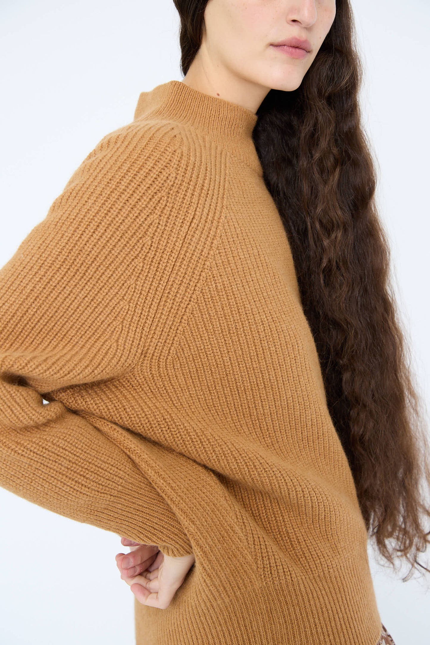 A person with long wavy hair wearing the Wool and Angora Ridge Knitted Pullover in Camel by Ichi Antiquités, standing against a plain background.