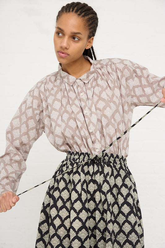 Woman in an Ichi Antiquités Woven Cotton Indian Block Print Shirt in Beige skirt made of Indian block print cotton, holding a bow without an arrow against a white background.