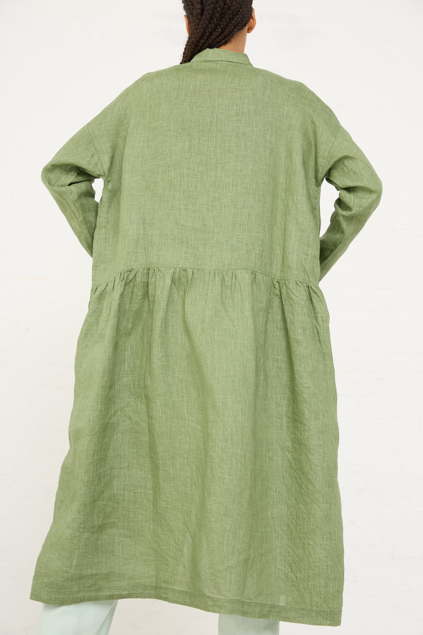 Woman standing with her back facing the camera, wearing a long, green, pigment-dyed Ichi Antiquités linen dress with a gathered waist.